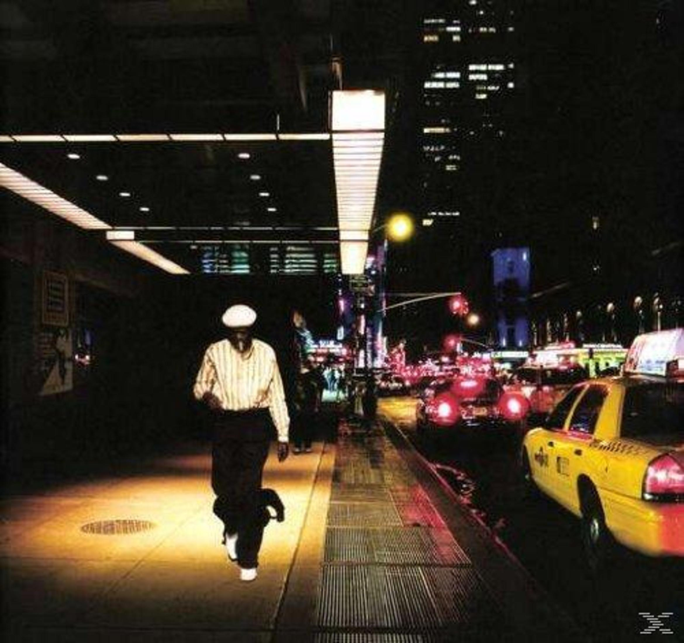 Un uomo in abiti a righe cammina su un marciapiede illuminato di notte.