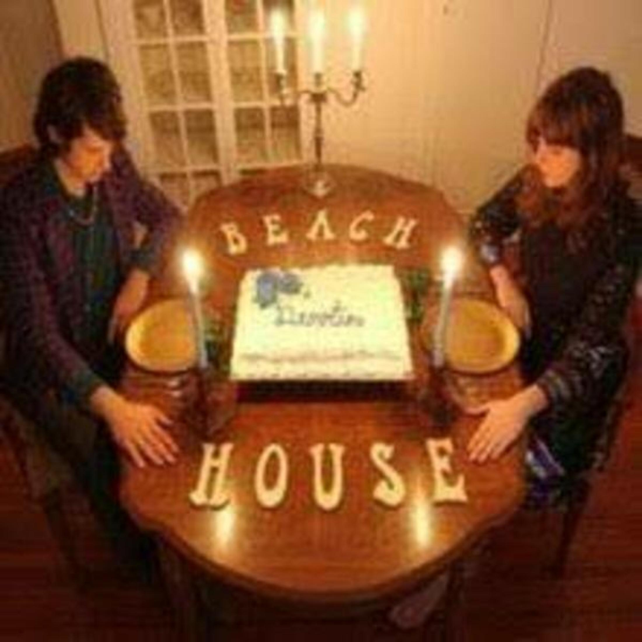 Due persone a tavola con torta, candele e le parole "BEACH HOUSE".