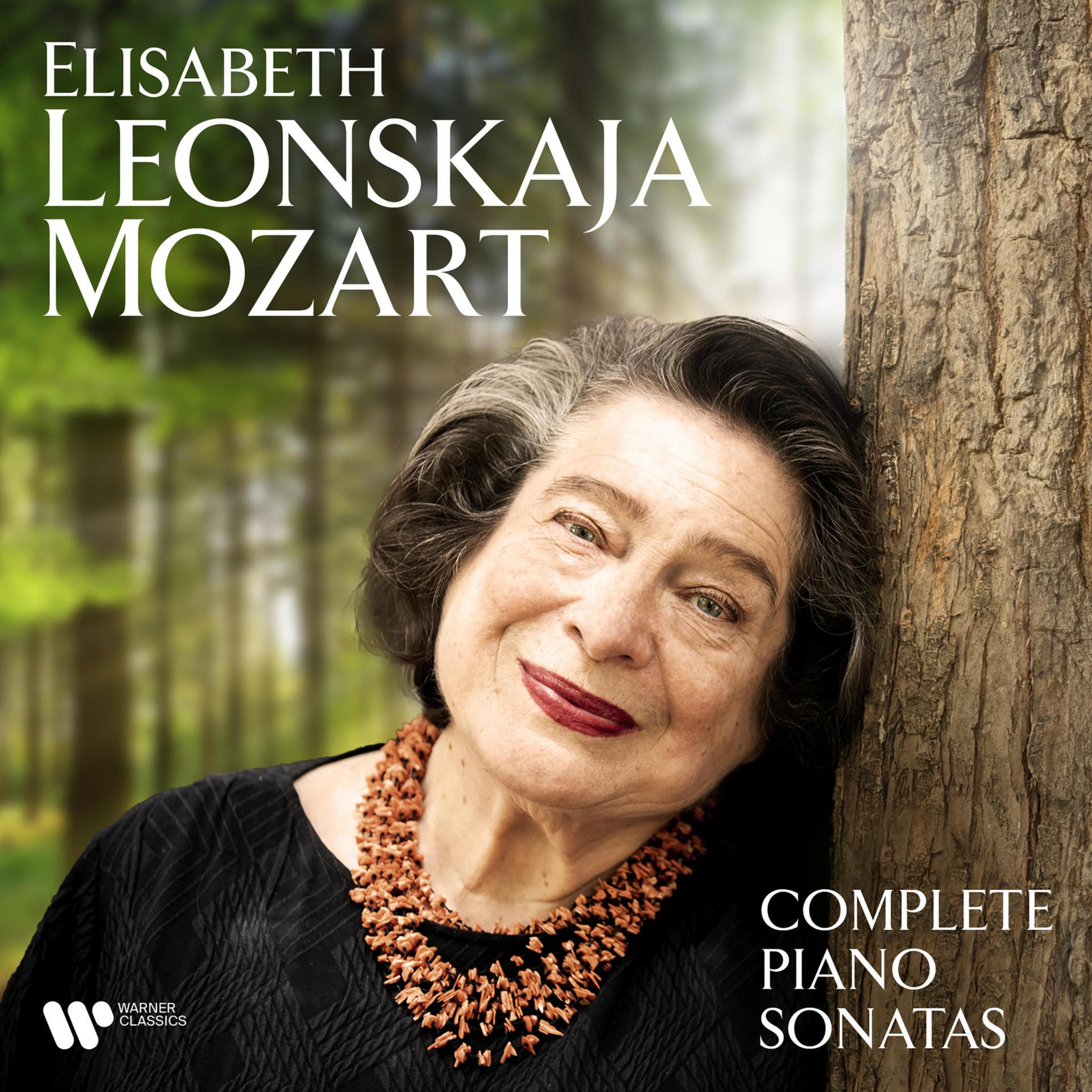 Elisabeth Leonskaja si appoggia a un albero. Indossa una collana di corallo. Bosco sullo sfondo.