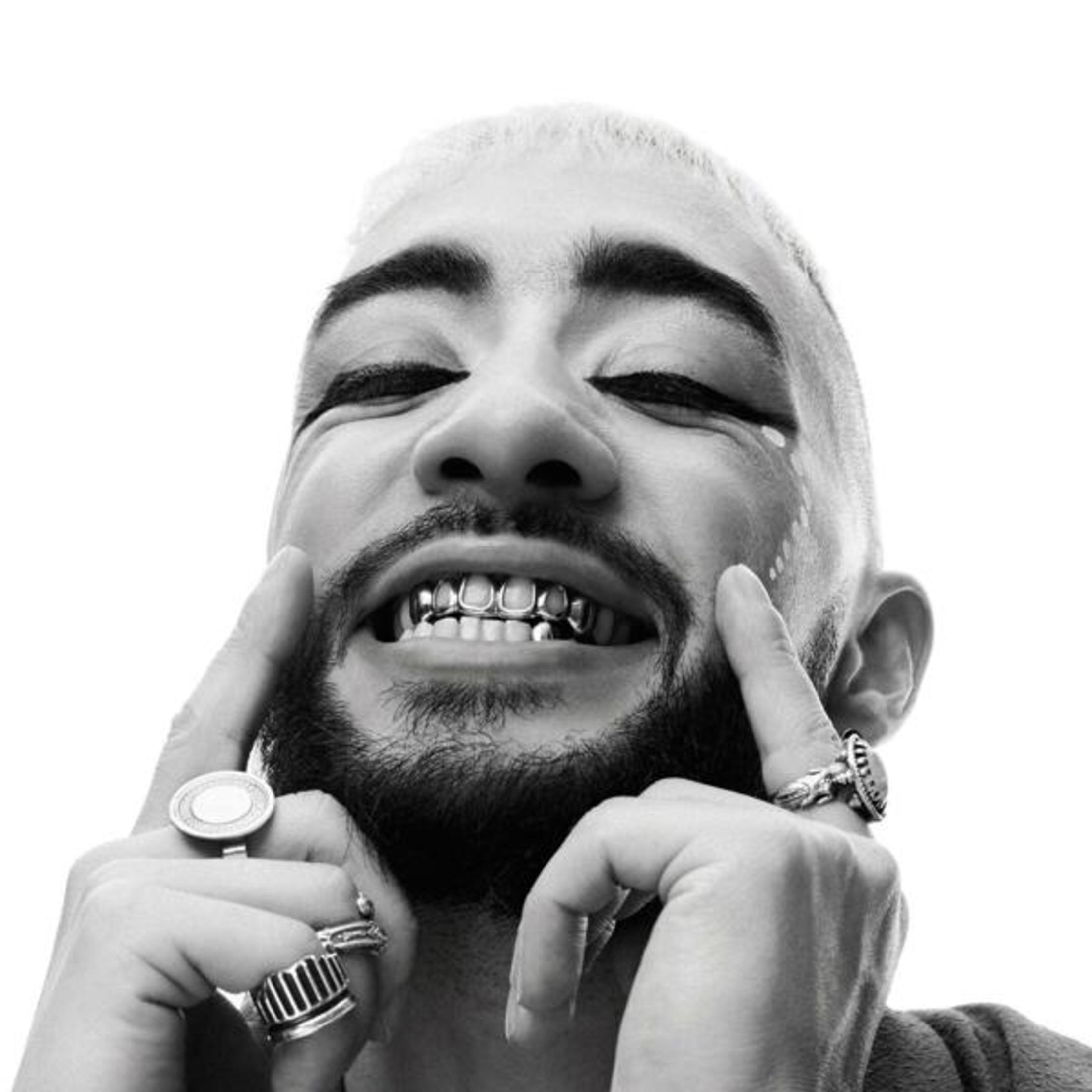 Ritratto in bianco e nero di un uomo con capelli biondi, grillz e anelli.