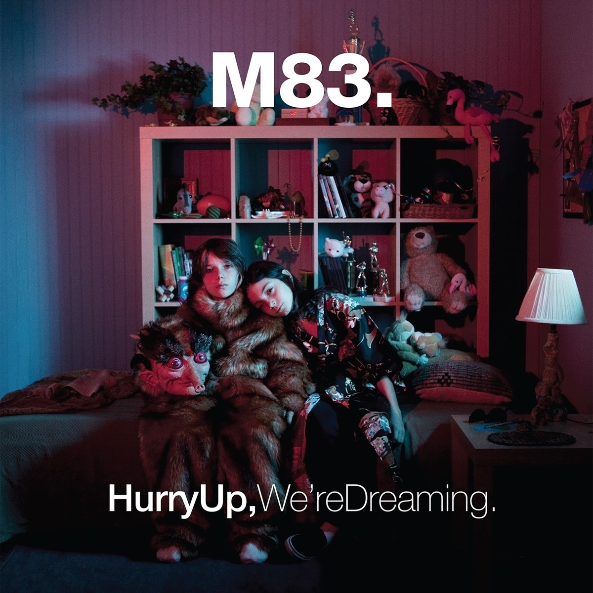 Due persone in pelliccia sedute davanti a una mensola di giocattoli. M83. HurryUp, We're Dreaming.