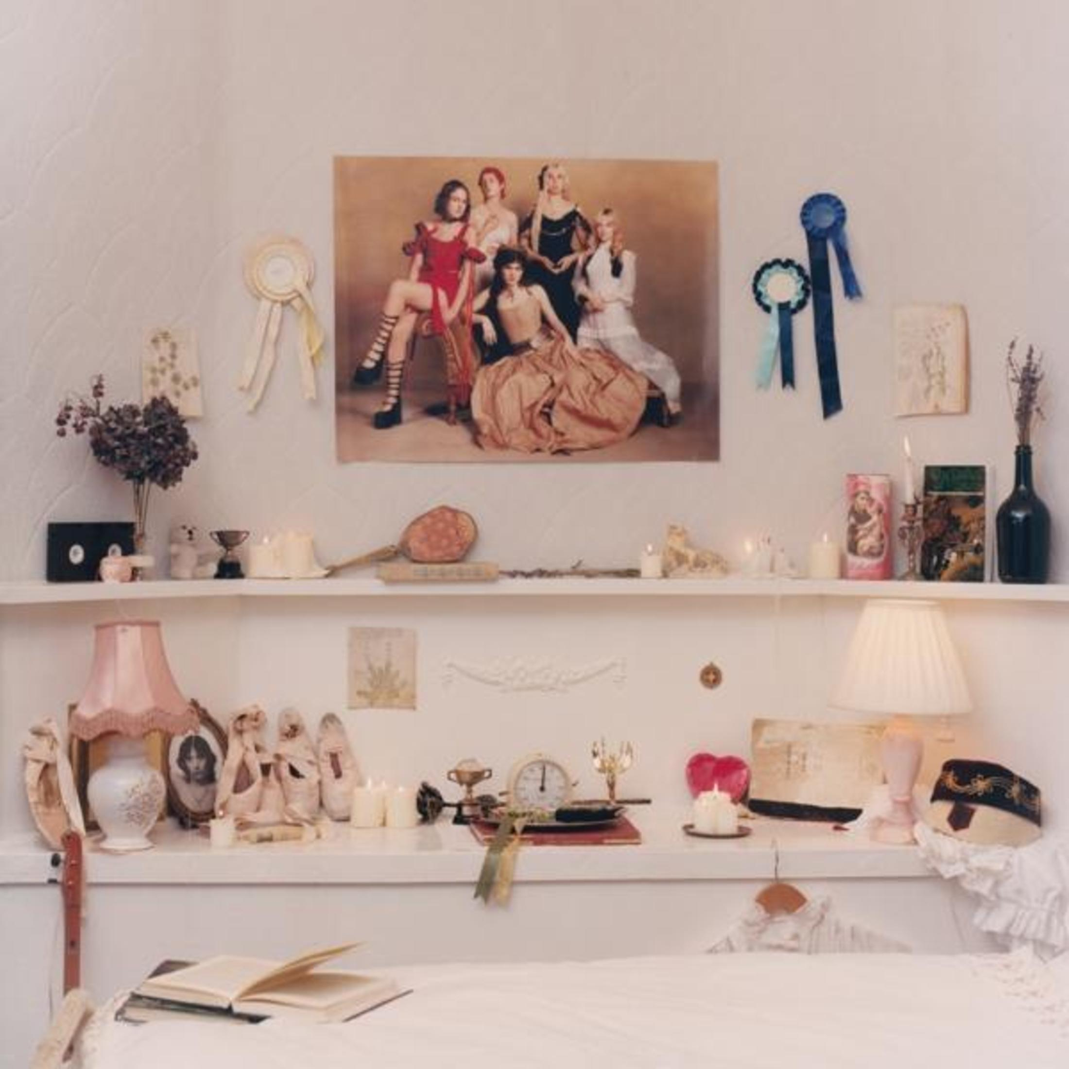 Un quadro di cinque donne, un libro, una lampada e un vaso di fiori.