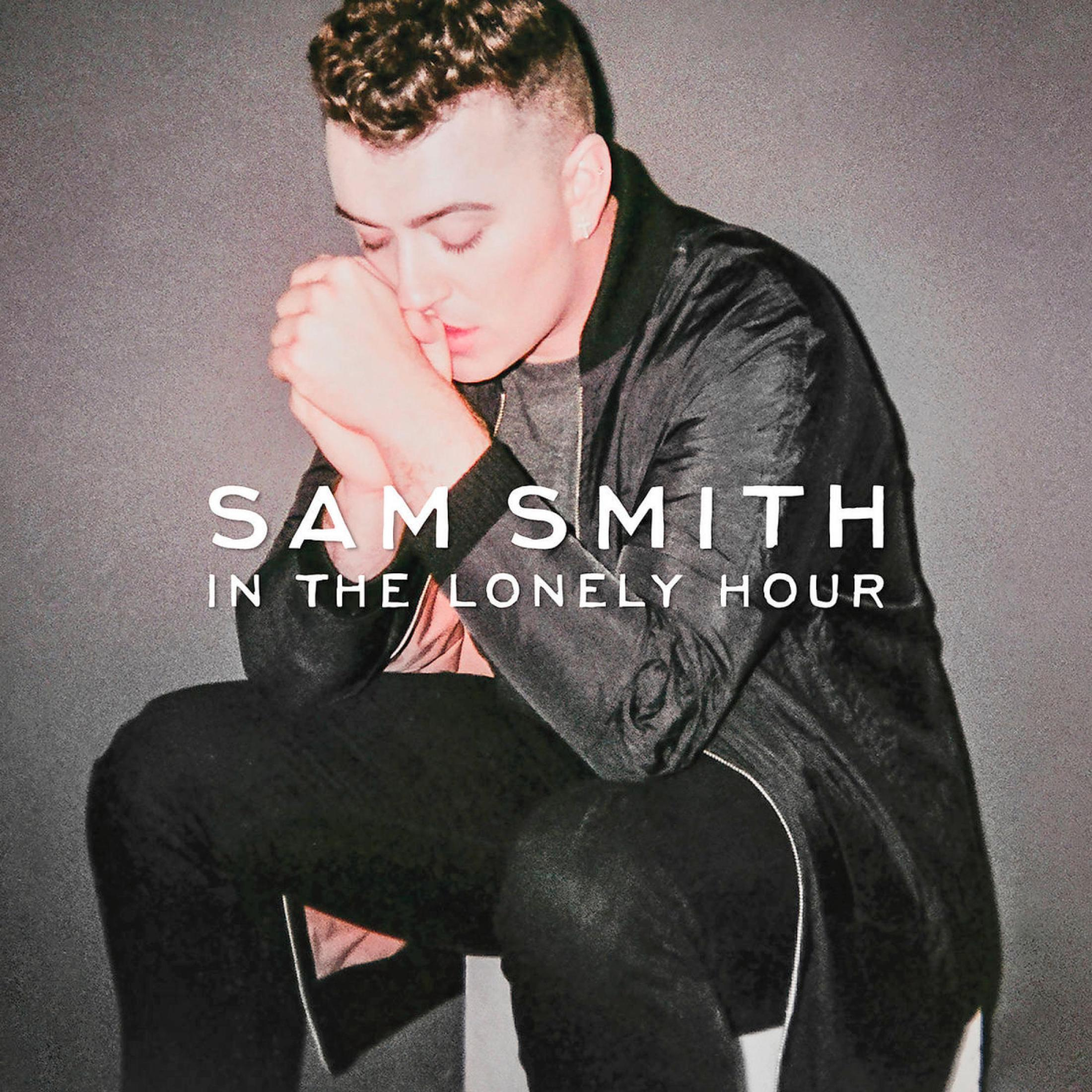 Sam Smith è seduto con la mano alla bocca su sfondo grigio.