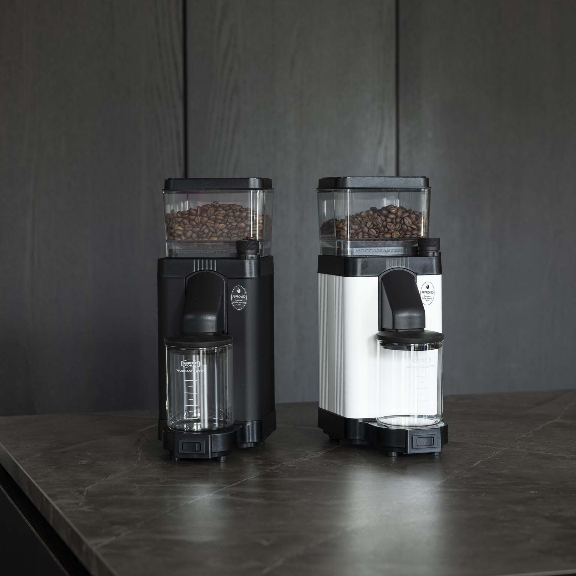Zwei Kaffeemühlen: eine schwarze und eine silberne, beide gefüllt mit Kaffeebohnen.