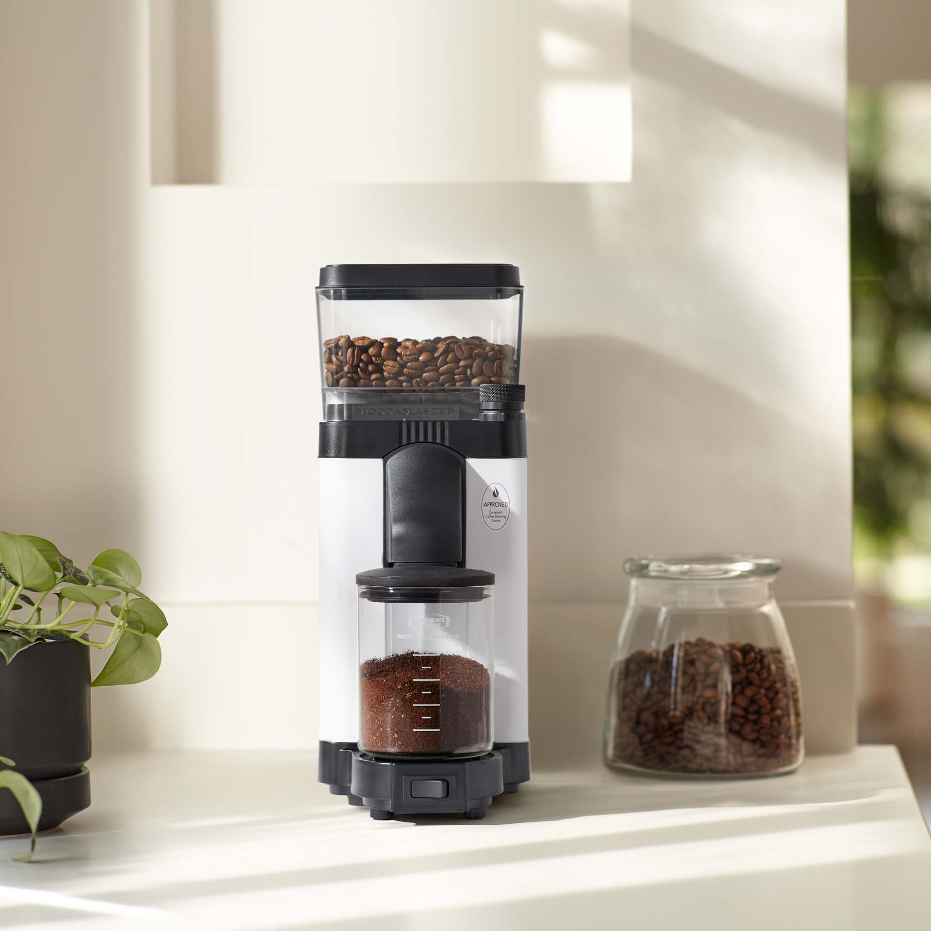 Ein weißer Kaffeemühle mit Kaffeebohnen oben und gemahlenem Kaffee unten.