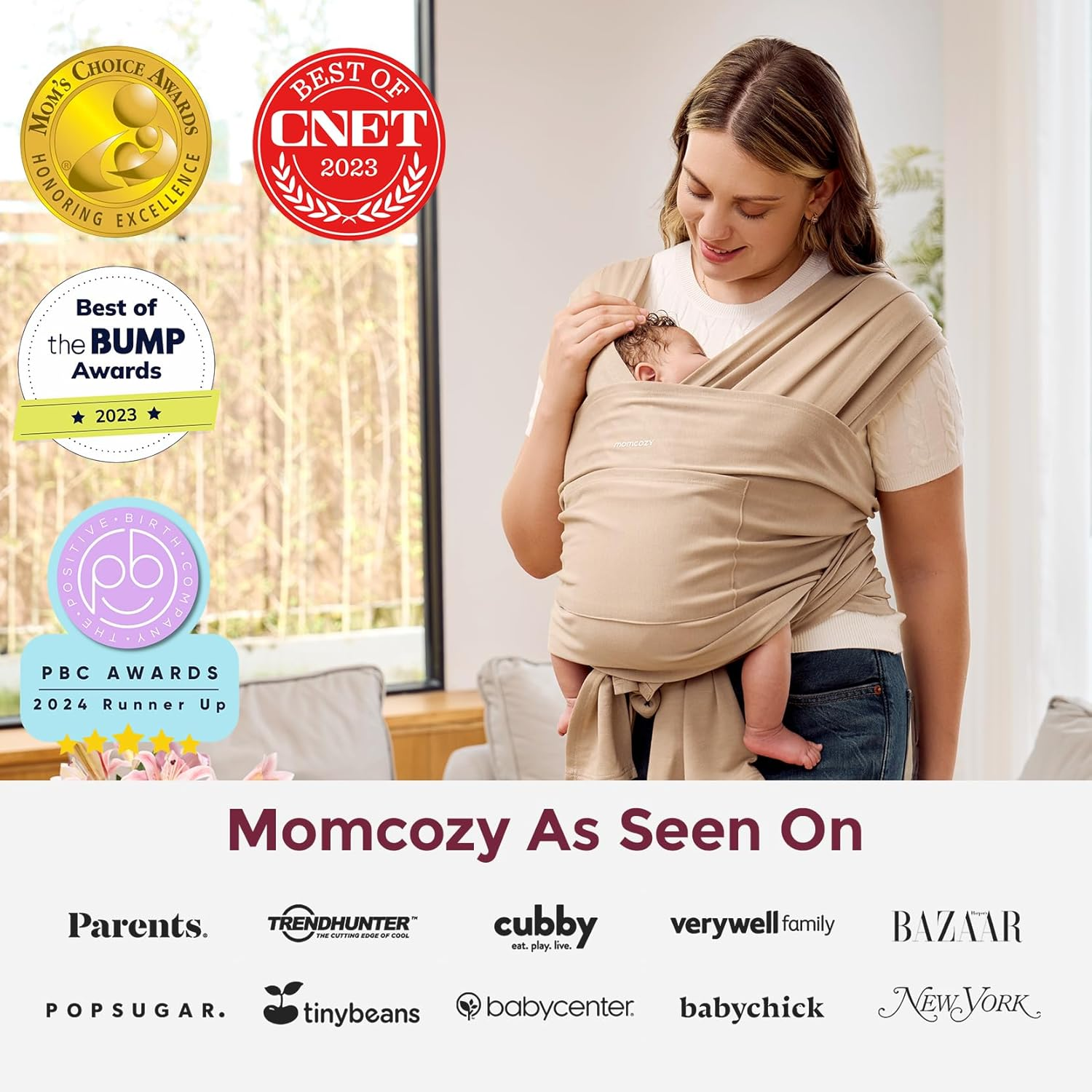 Mama nosi dziecko w beżowym nosidełku, otoczona nagrodami i logotypami.