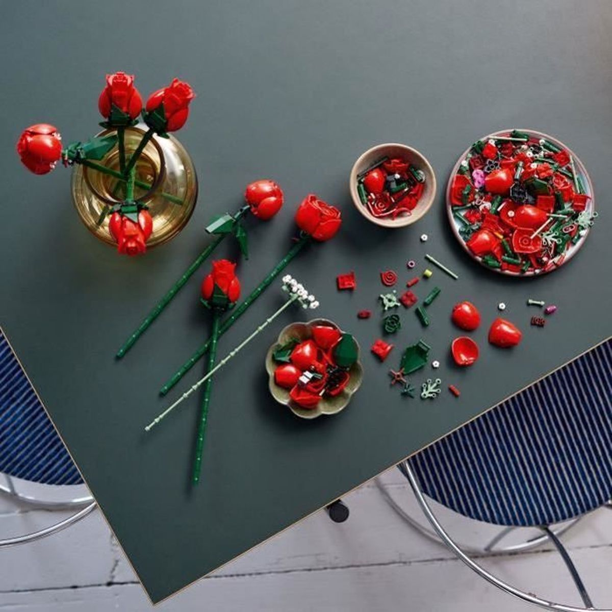 Rode Lego rozen in en rond een vaas, op een tafel met bouwstukken.