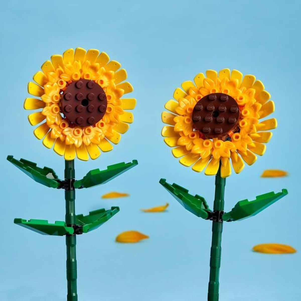 Mavi gökyüzüne karşı sarı yapraklı, kahverengi merkezli iki LEGO ayçiçeği.