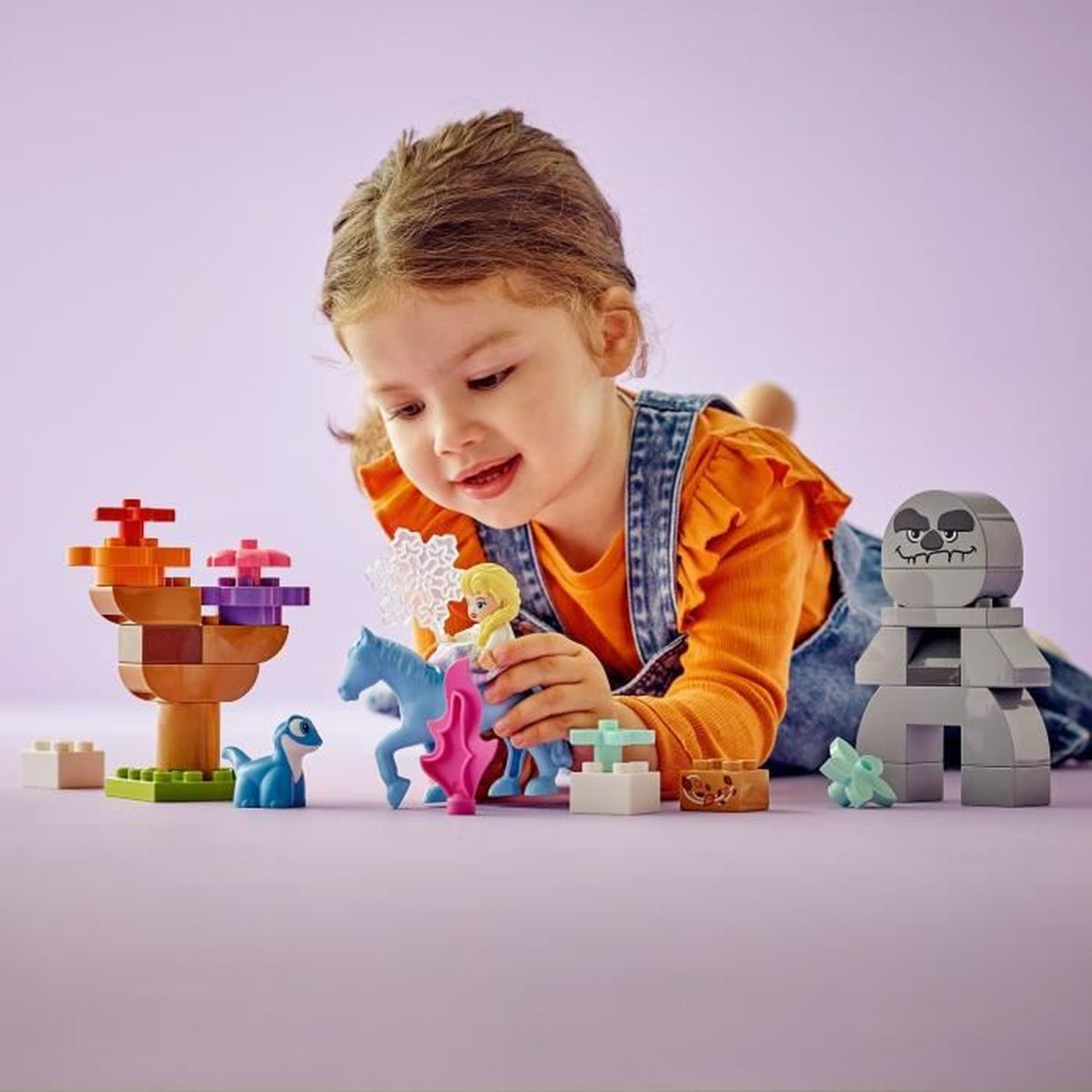 Mała dziewczynka bawi się figurkami Lego: Elsa na koniu, dinozaur, kamienna istota.