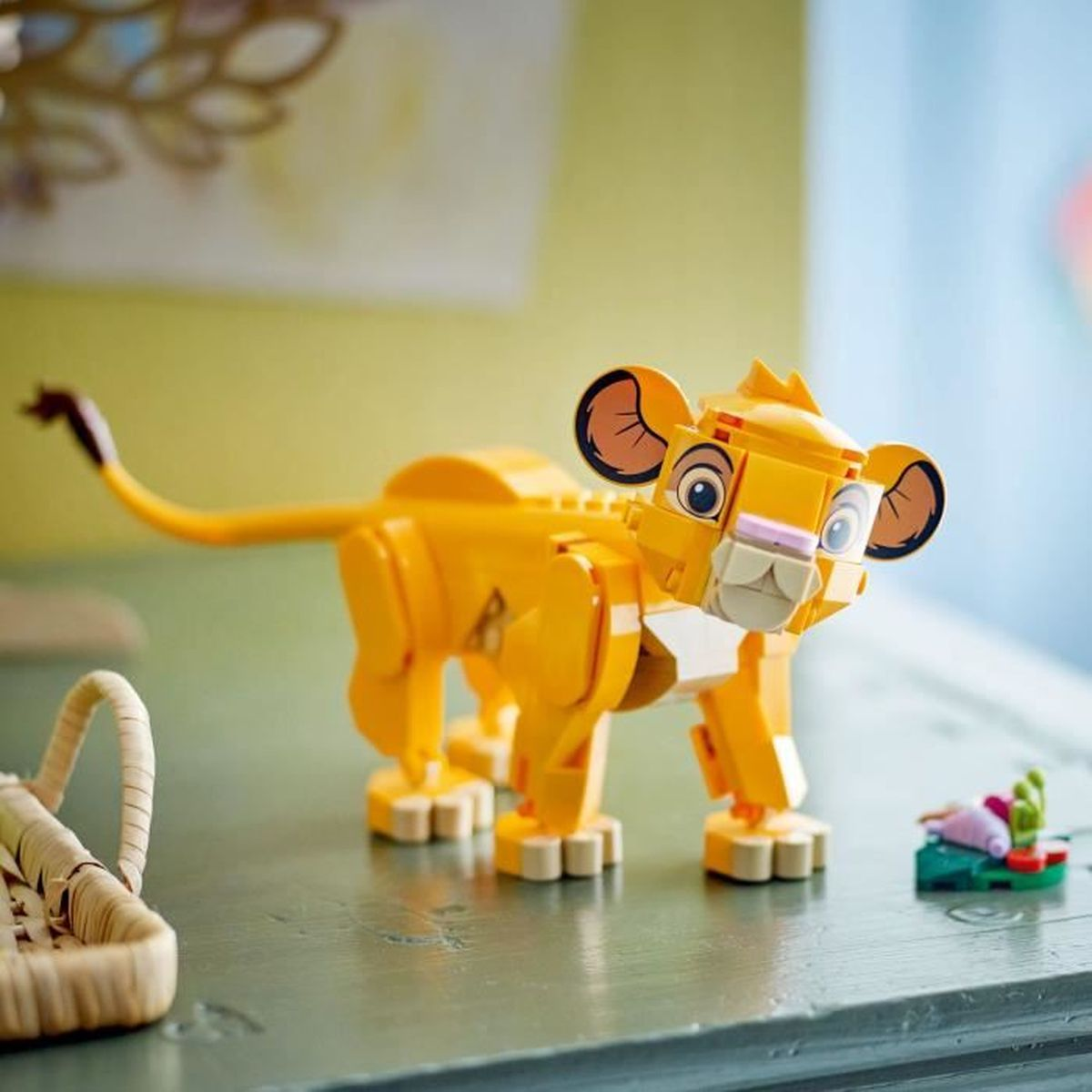 Un león Lego amarillo con orejas grandes está sobre una mesa junto a una cesta.