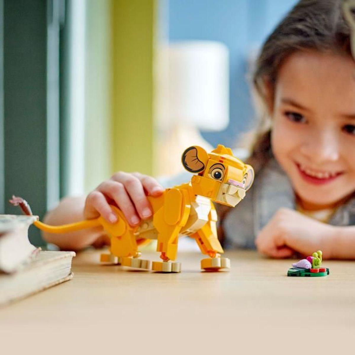 Un niño juega con un león de Lego amarillo y un pequeño insecto en una mesa de madera.