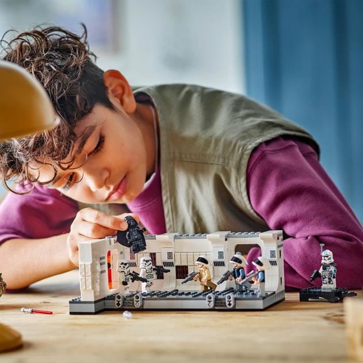 Chłopiec buduje zestaw Lego z figurkami Gwiezdnych Wojen na drewnianym stole.