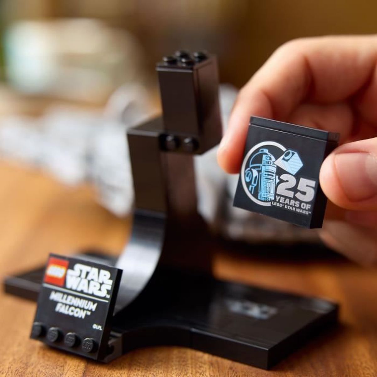 Dłoń trzyma czarny klocek LEGO z R2-D2 i napisem „25 lat LEGO Star Wars".