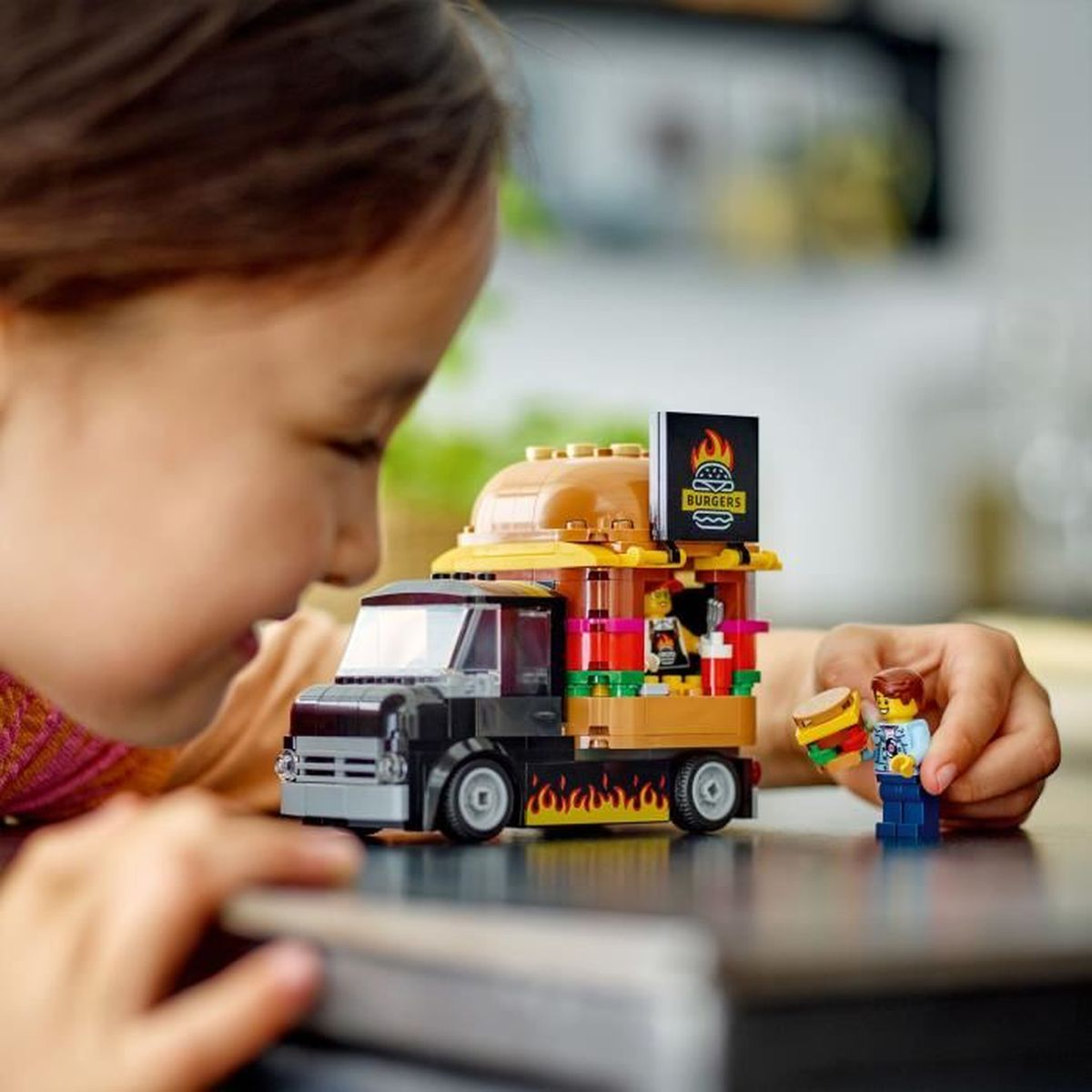 Niño juega con camión de hamburguesas Lego. Una figura sostiene una hamburguesa.