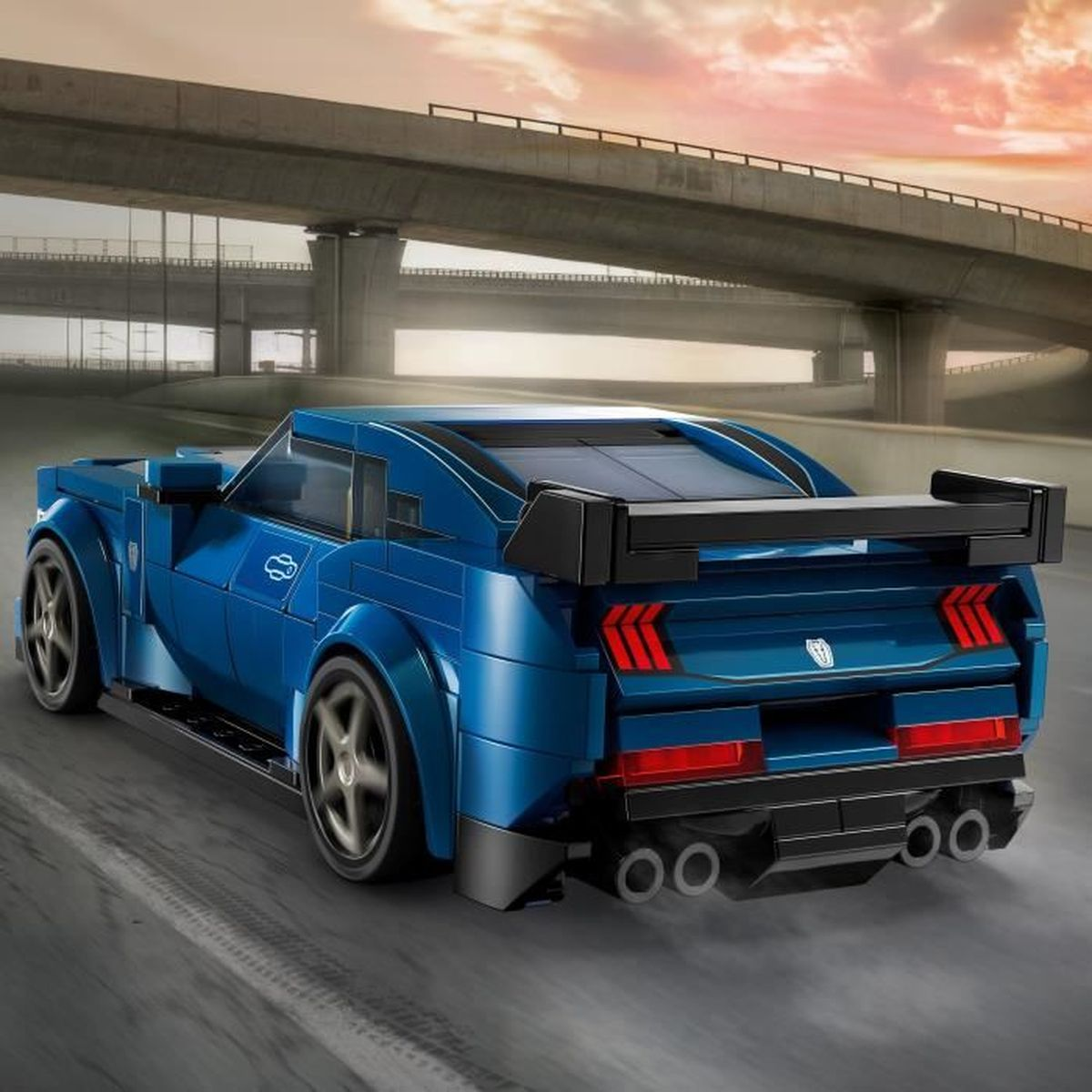 Niebieski samochód sportowy Lego ze spojlerem jedzie drogą pod wiaduktem.
