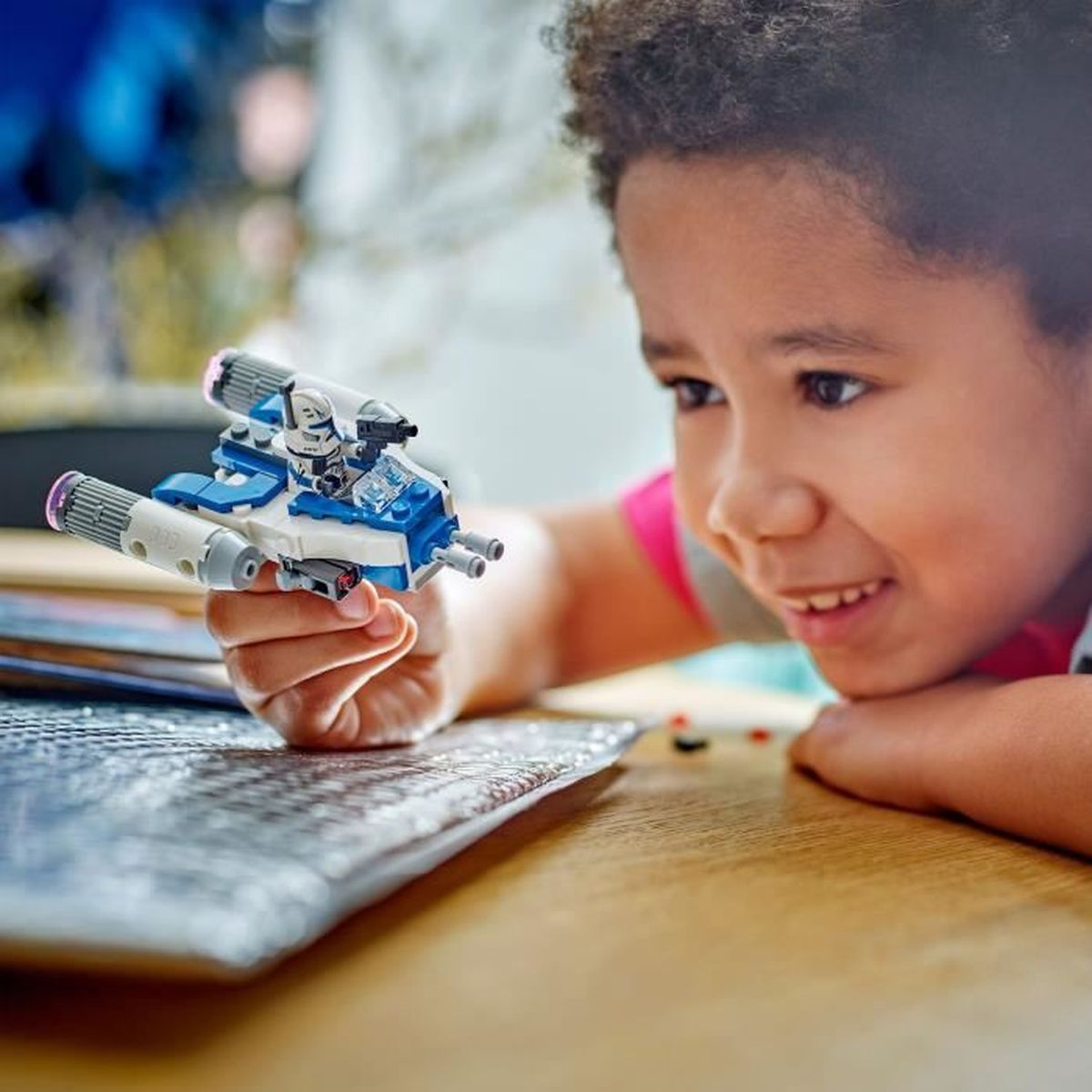 Bir çocuk, minifigür pilotlu mavi ve beyaz bir Lego uzay gemisi tutuyor.
