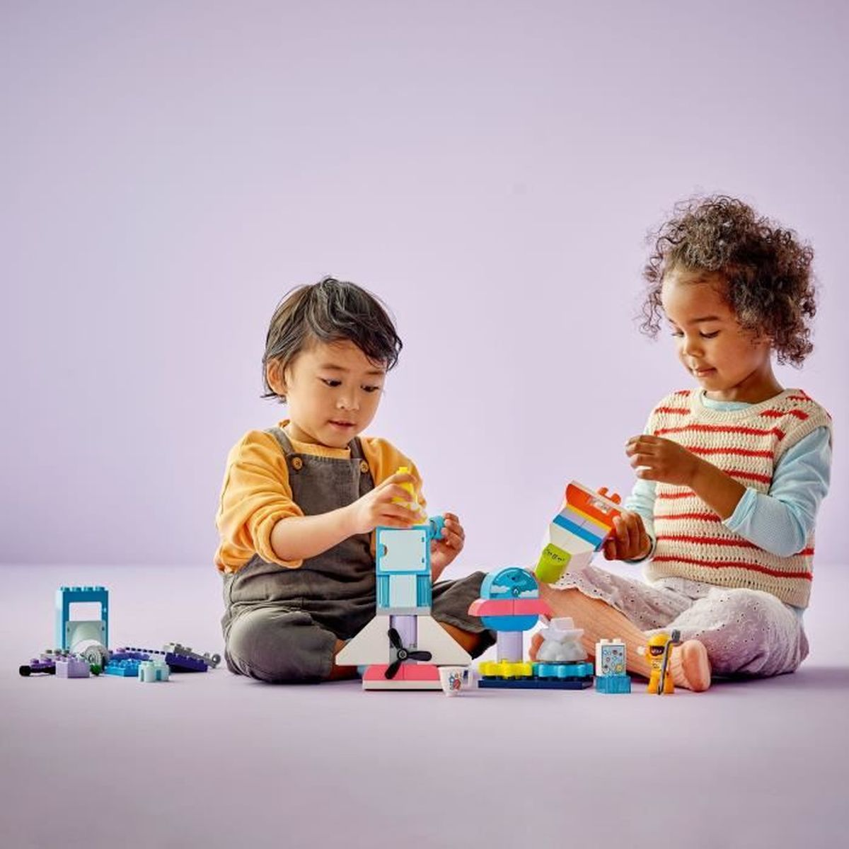 Dwoje dzieci bawi się kolorowymi klockami na fioletowym tle.