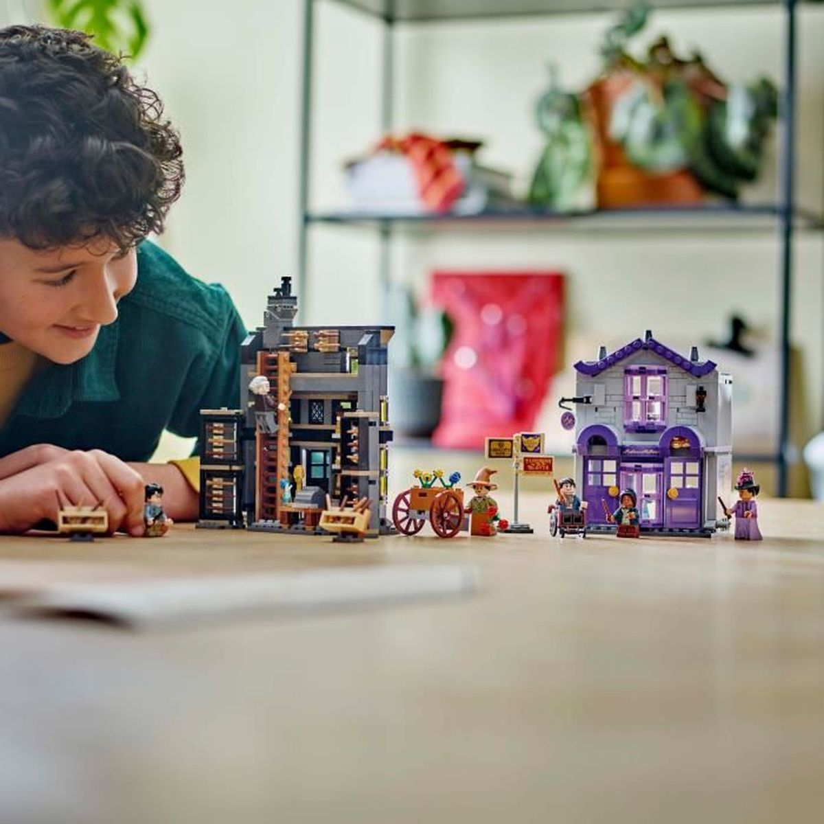 Un ragazzo costruisce modelli Lego di edifici e figure su un tavolo di legno.