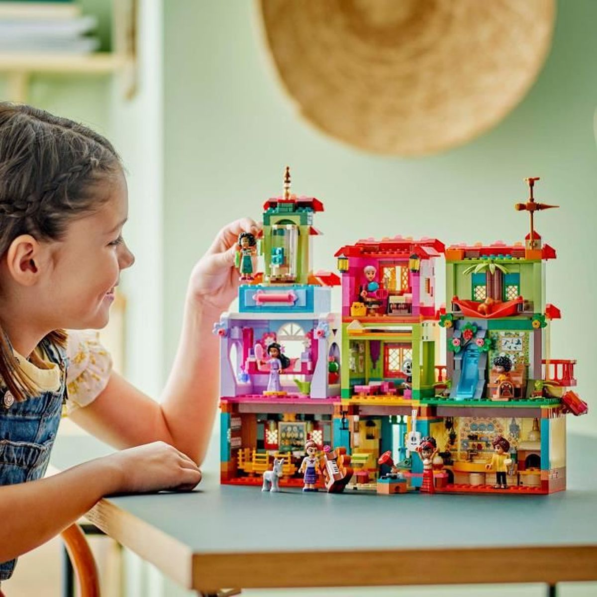 Ein Mädchen spielt mit einem bunten Lego-Hausmodell mit vielen kleinen Figuren und Details.