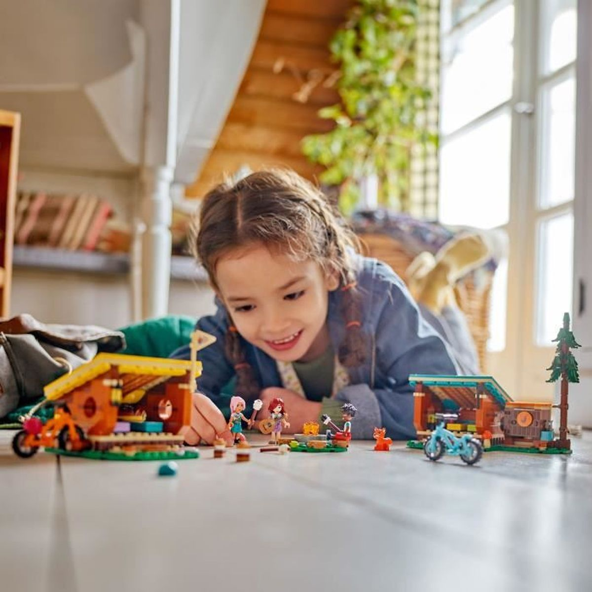 Dziewczynka bawi się klockami LEGO: domek, figurki, rowery i lis na drewnianej podłodze.