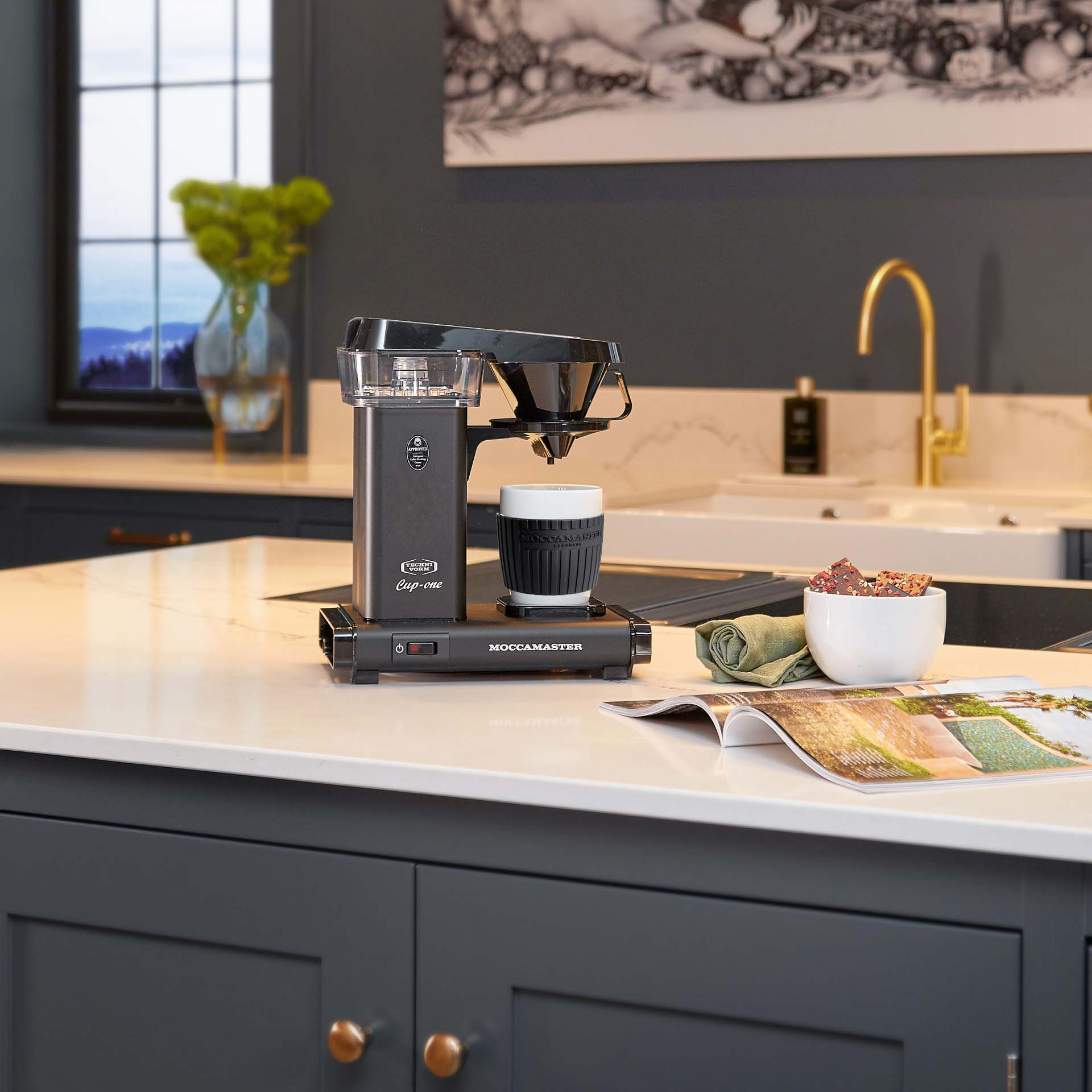 A black coffee maker sits on a kitchen counter with a cup.