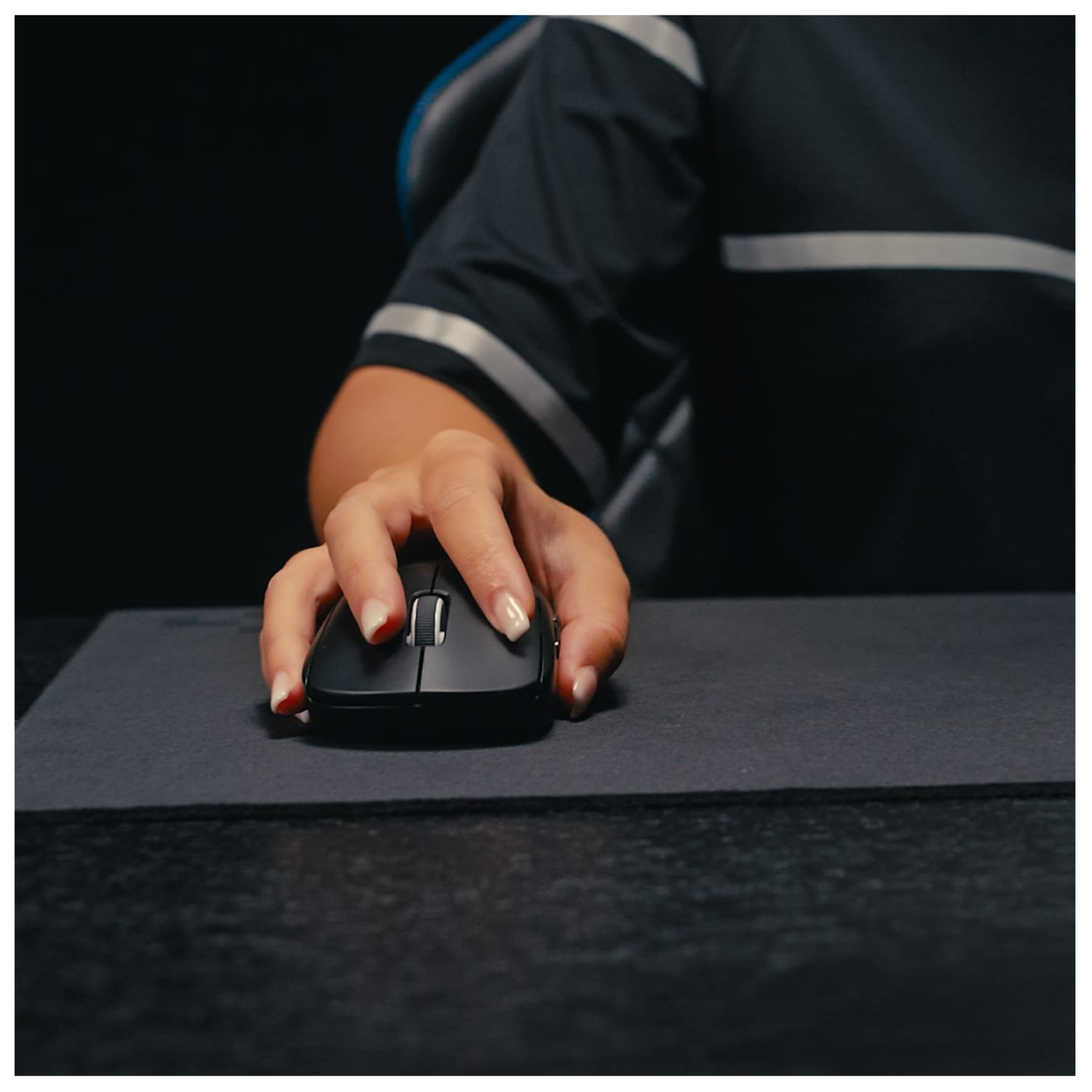Eine Hand bedient eine schwarze Computermaus auf einer dunklen Matte.