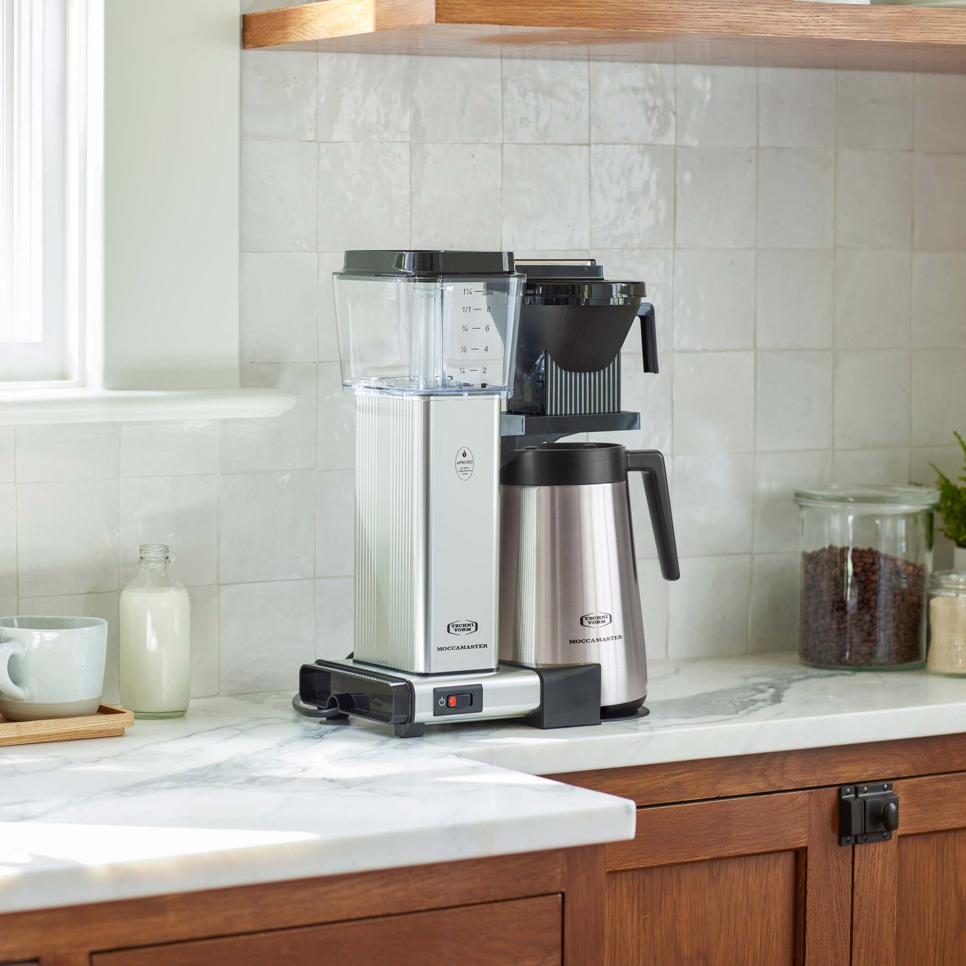 Une cafetière Moccamaster argentée avec carafe isotherme sur un comptoir en marbre.