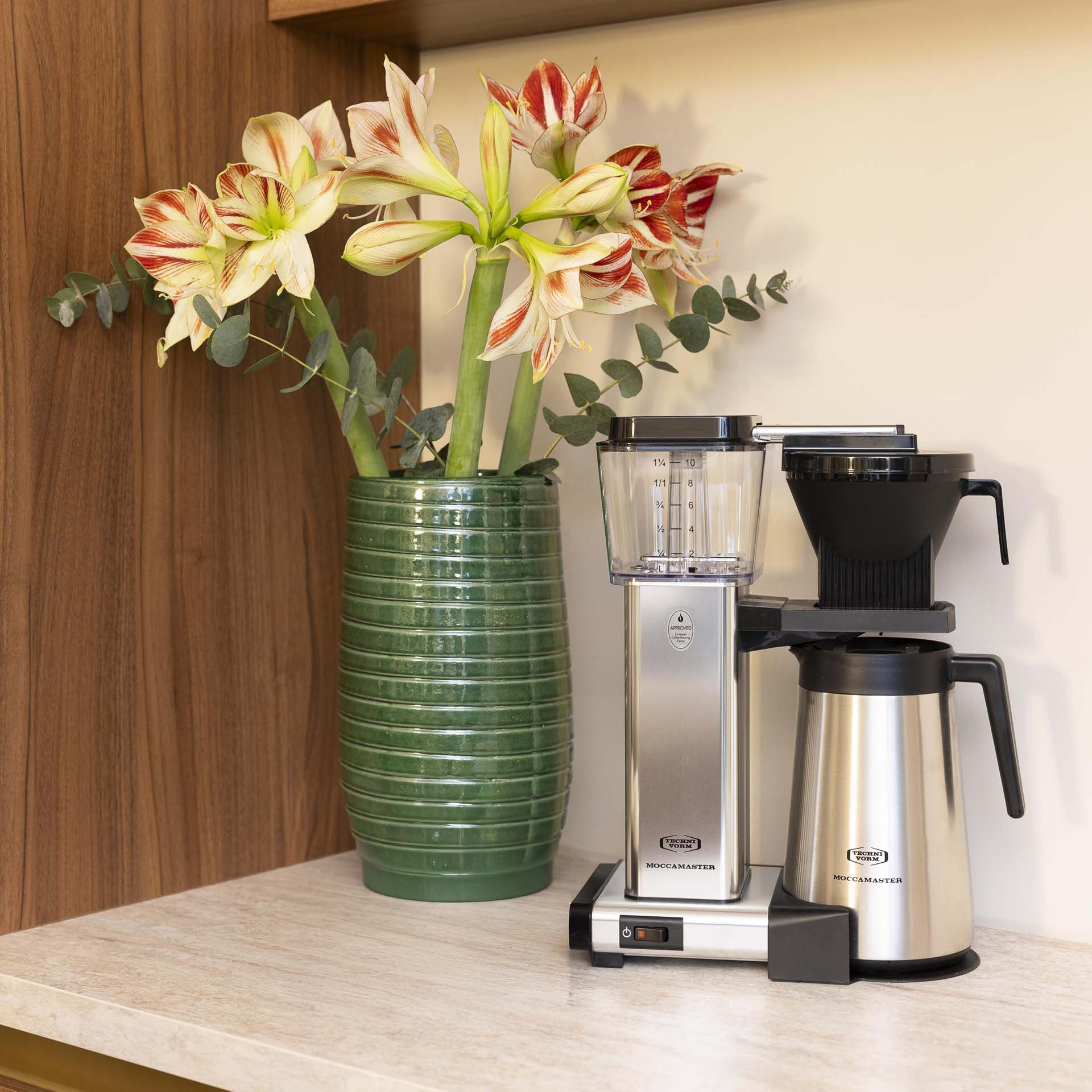 Machine à café à côté d'un vase vert avec des fleurs rayées.
