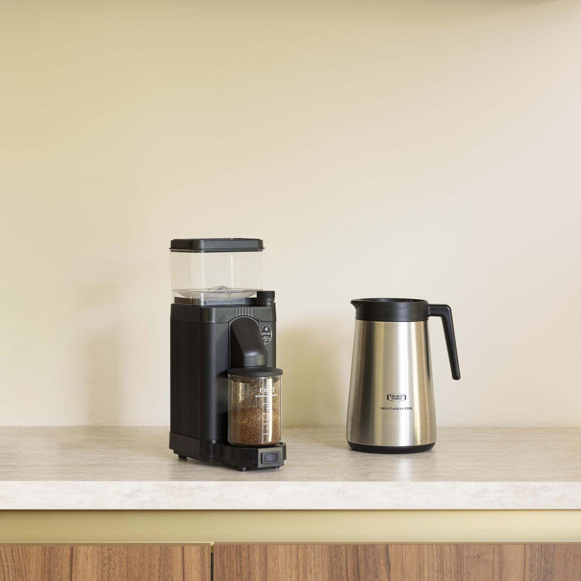 Schwarzer Kaffeevollautomat und silberne Thermoskanne auf einer Arbeitsplatte.