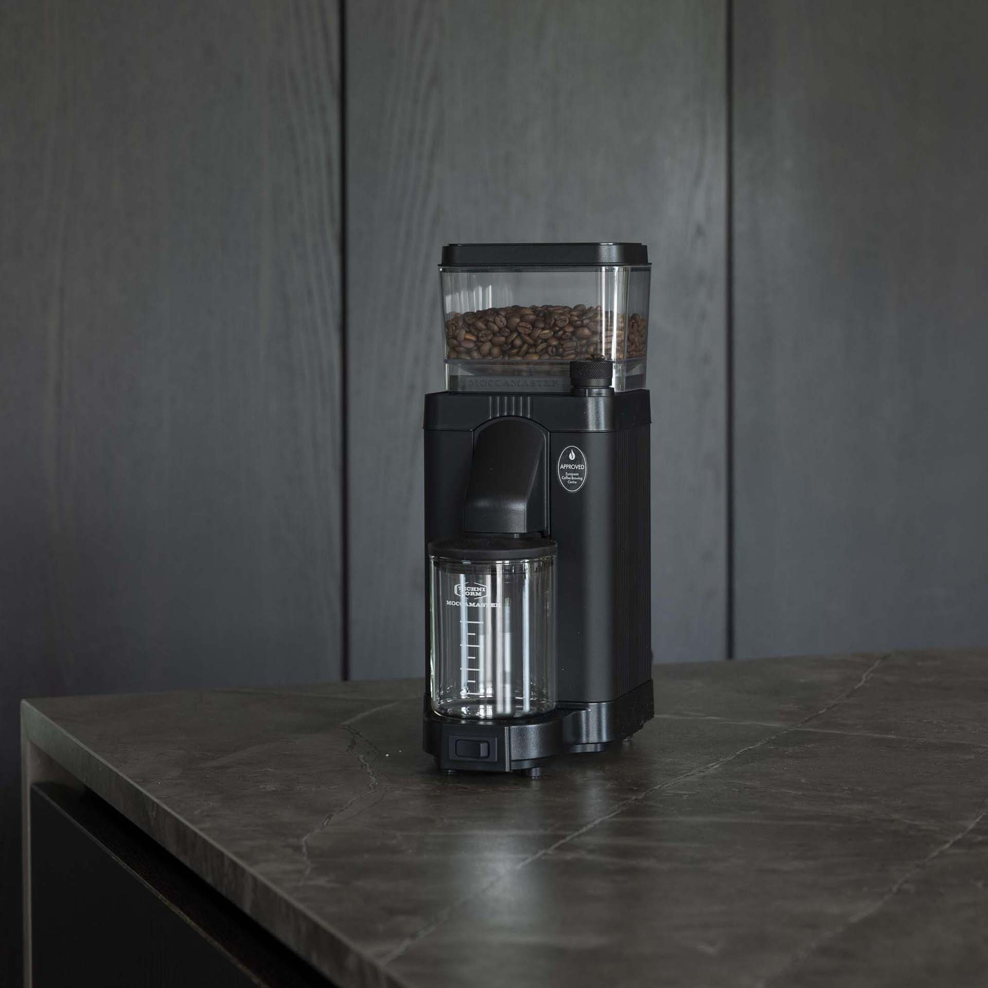 Schwarzer Kaffeemühle mit Bohnen im oberen Behälter und Glasbehälter unten.