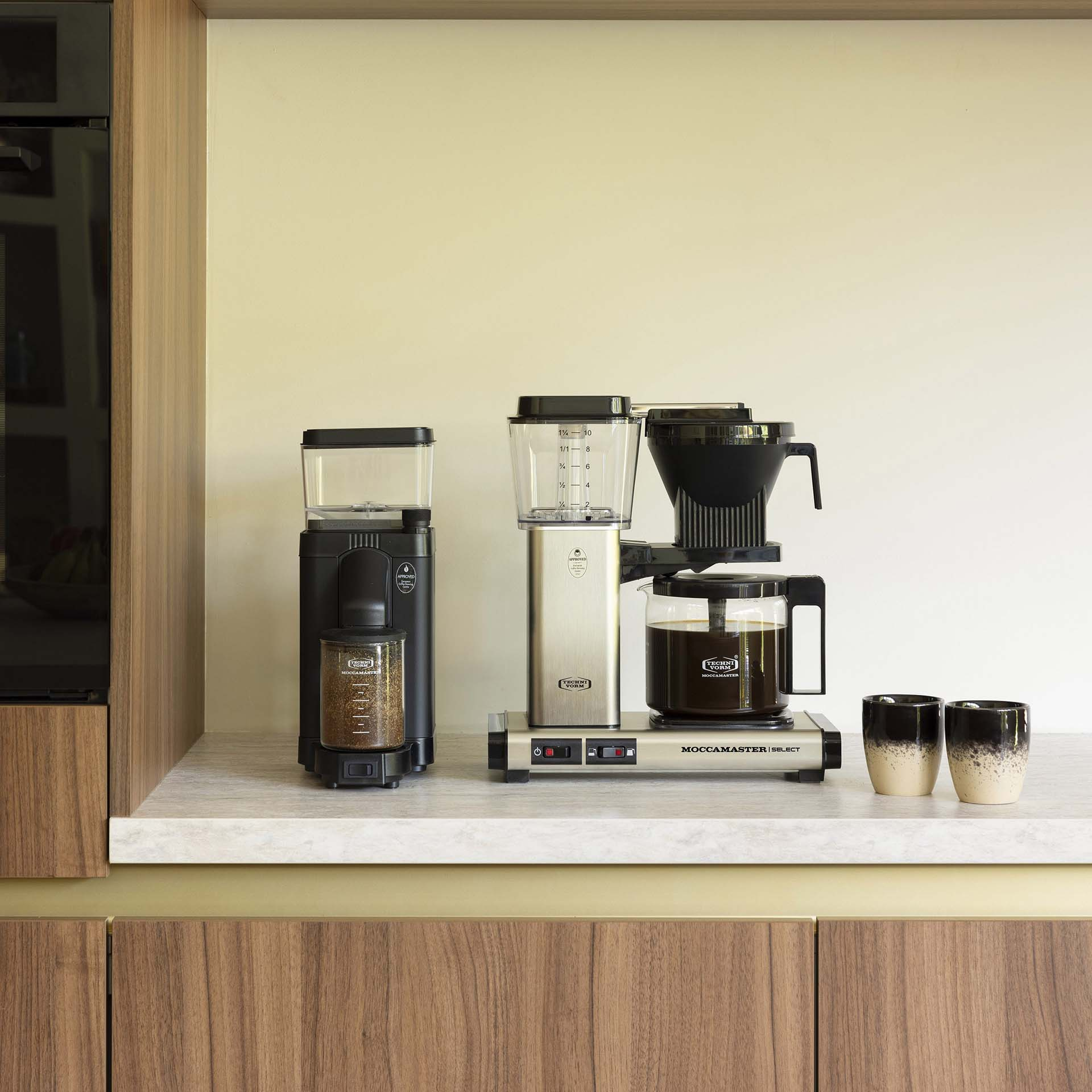 Zwei Kaffeemaschinen mit Glaskaraffen und zwei Tassen auf einer Arbeitsplatte.