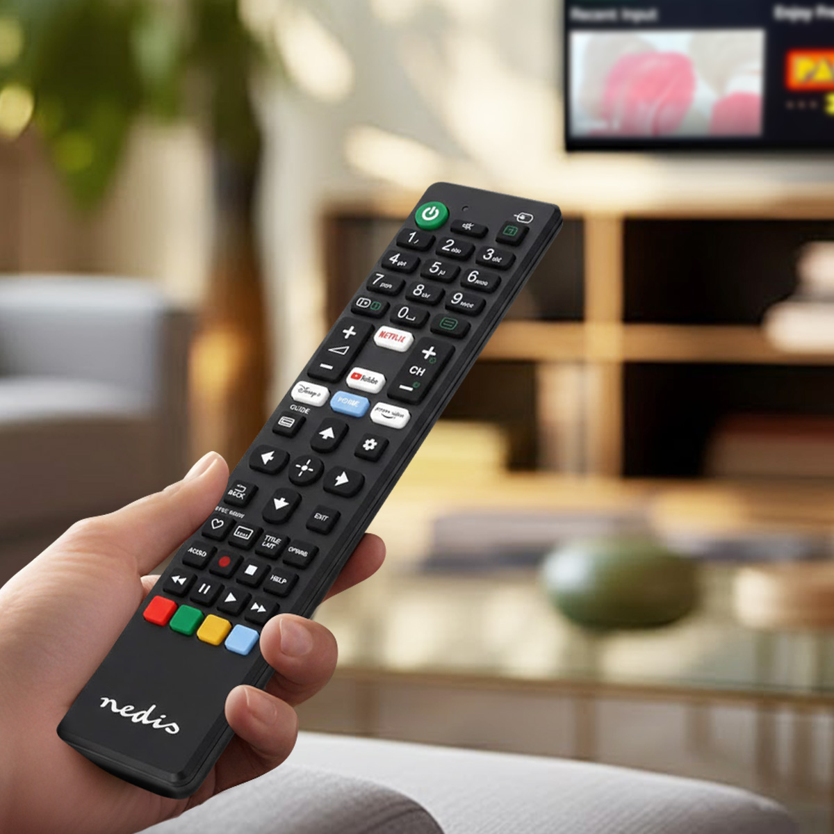 Ręka trzyma czarny pilot z wieloma przyciskami, w tym skrótami do aplikacji.