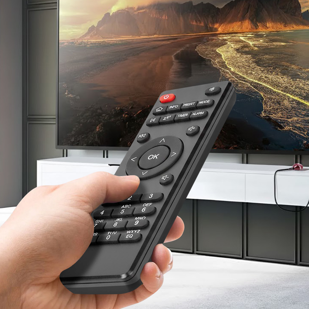 Dłoń trzyma czarny pilot przed dużym telewizorem wyświetlającym krajobraz.