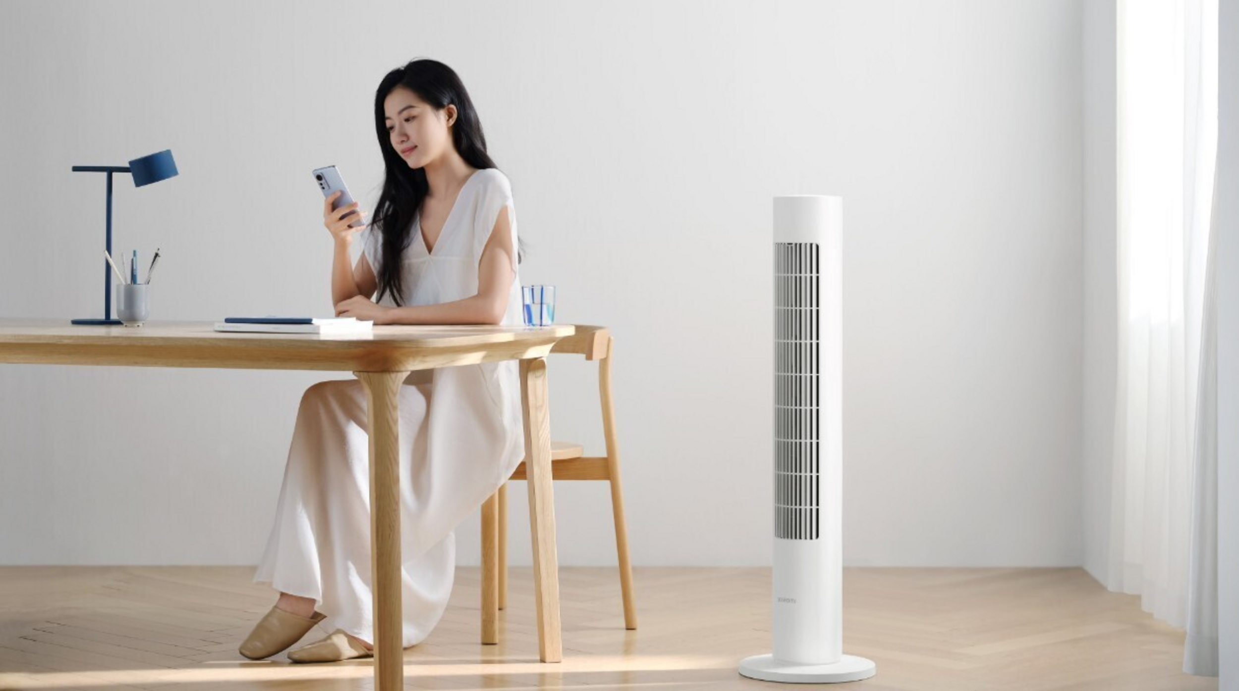 Kobieta przy biurku z telefonem, obok wentylator wieżowy.