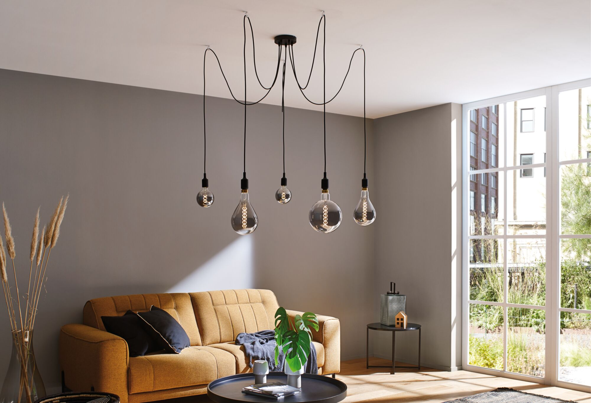 Ein Wohnzimmer mit einem senfgelben Sofa und fünf Hängeglühlampen.