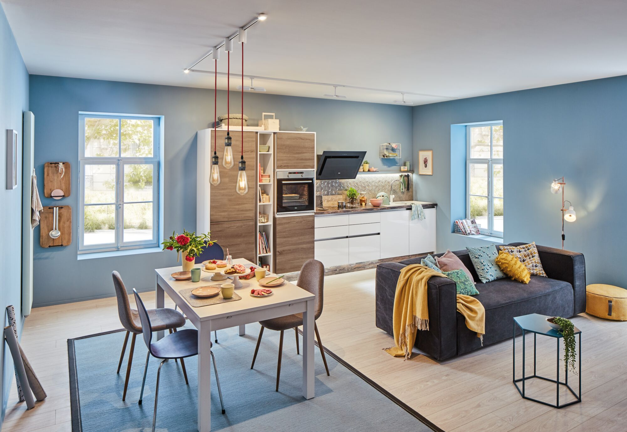 Otwarta strefa dzienna z jadalnią i kuchnią, niebieskie ściany, drewniana podłoga.