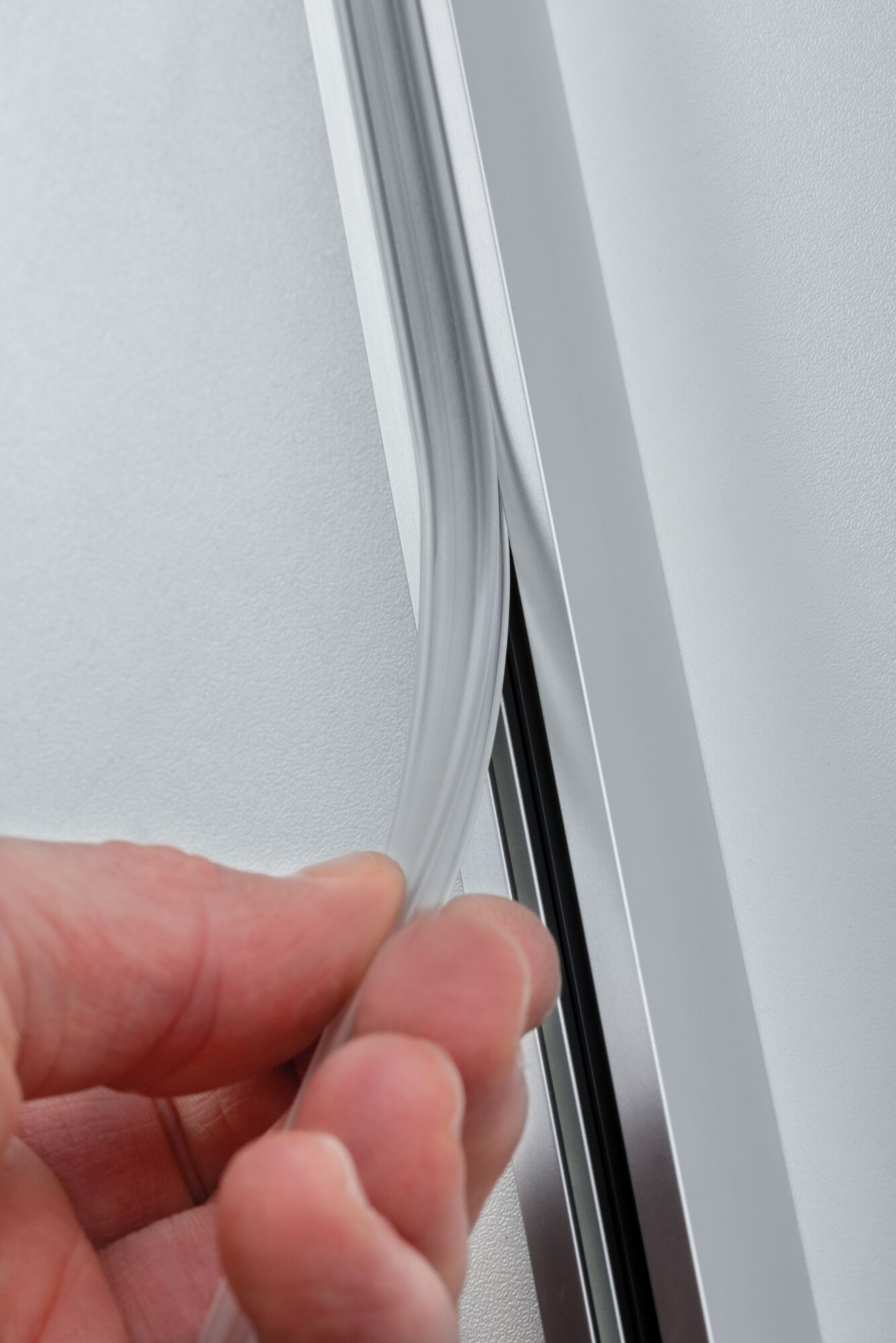 Eine Hand hält eine transparente Dichtung an einem Aluminiumprofil.