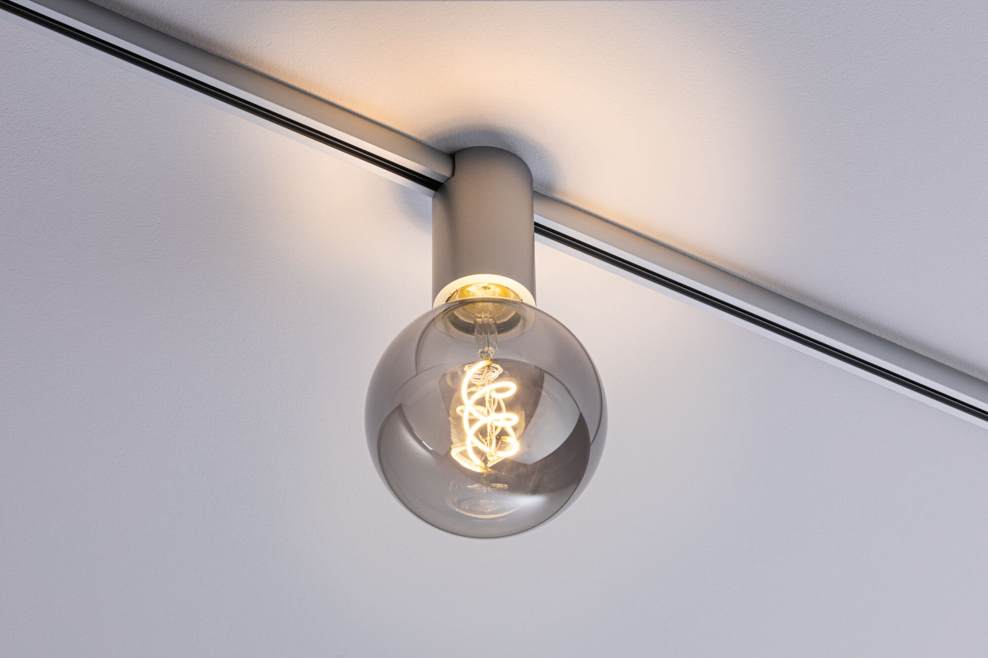 Eine graue Glühbirne mit Spiralwendel hängt an einer Schiene an der Decke.