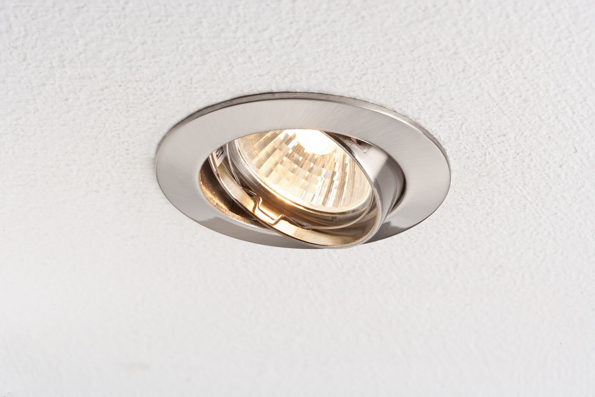 Ein Einbaustrahler mit silbernem Gehäuse leuchtet auf einer weißen Decke.