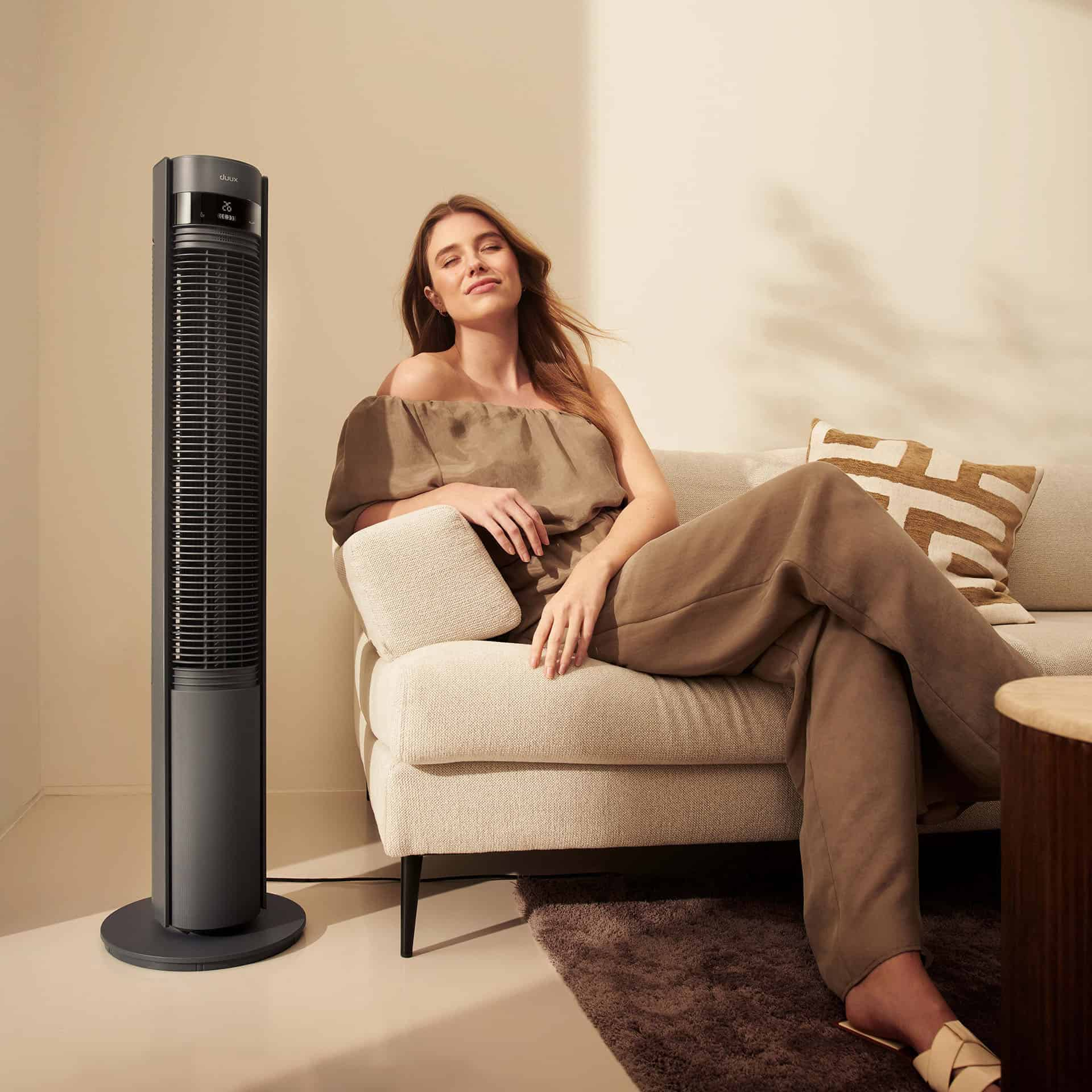 Eine Frau sitzt auf einem Sofa neben einem Turmventilator.