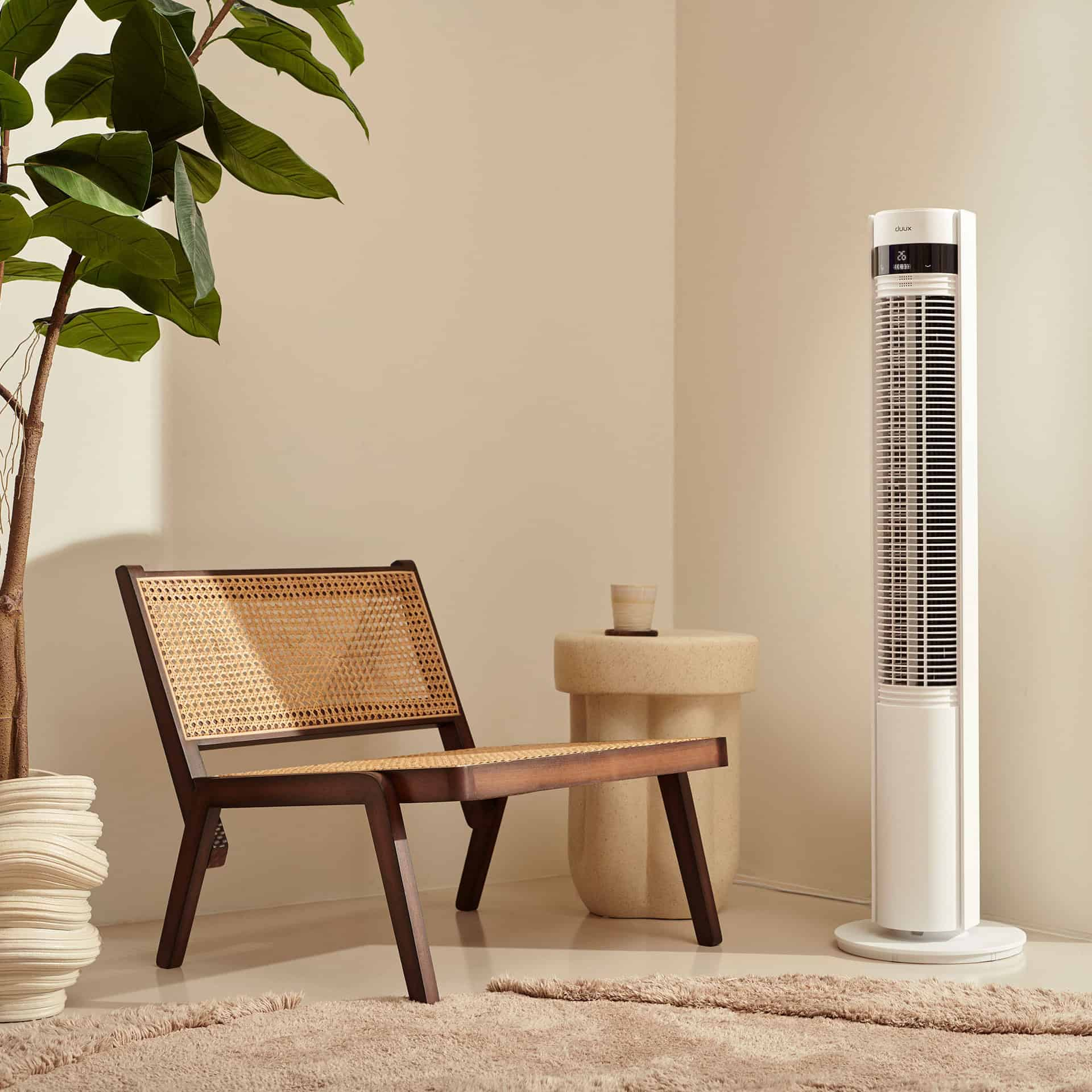 Ein weißer Turmventilator steht neben einem braunen Rattan-Stuhl und einer Pflanze.