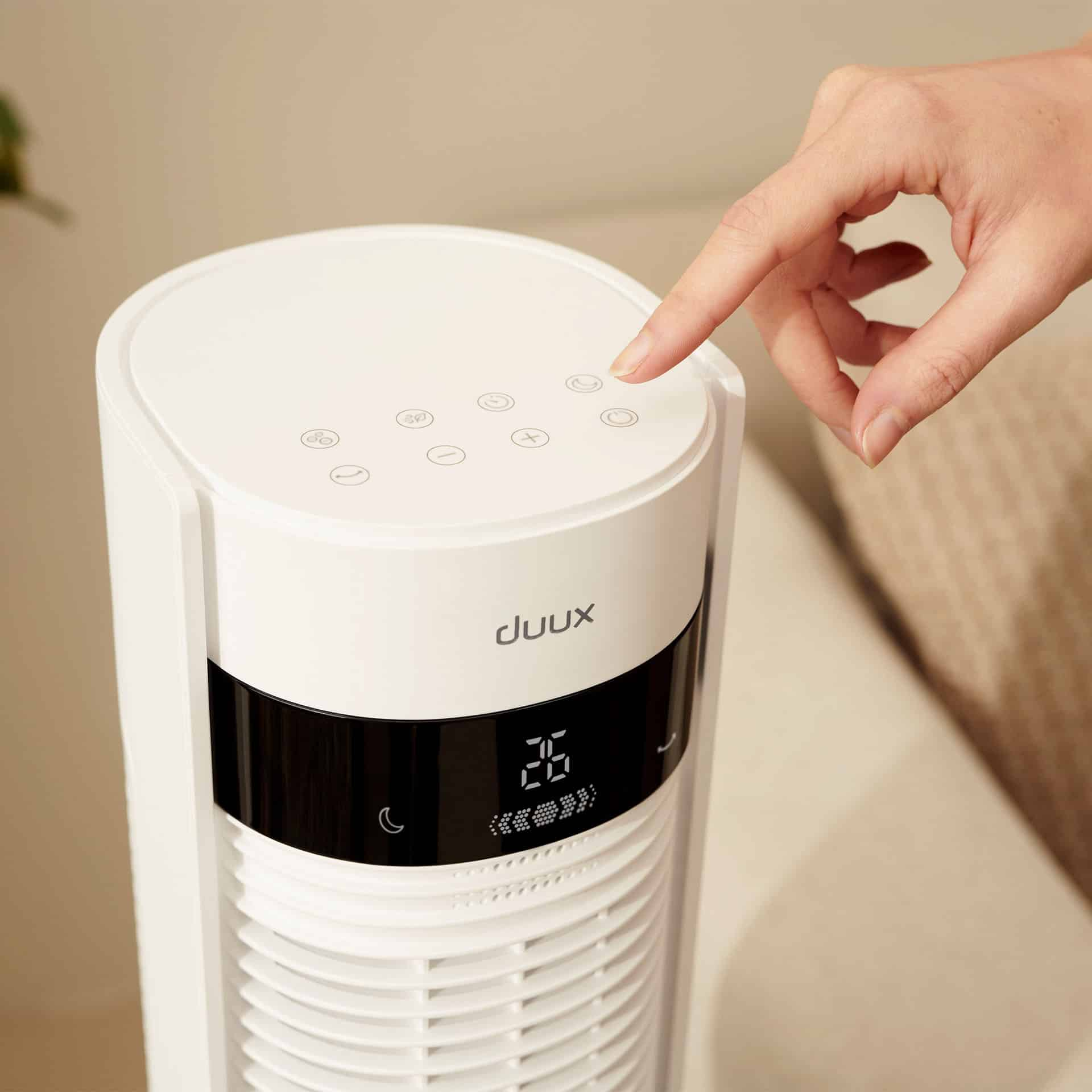 Ein Finger drückt einen Knopf an einem weißen Duux Turmventilator mit Digitalanzeige 26.