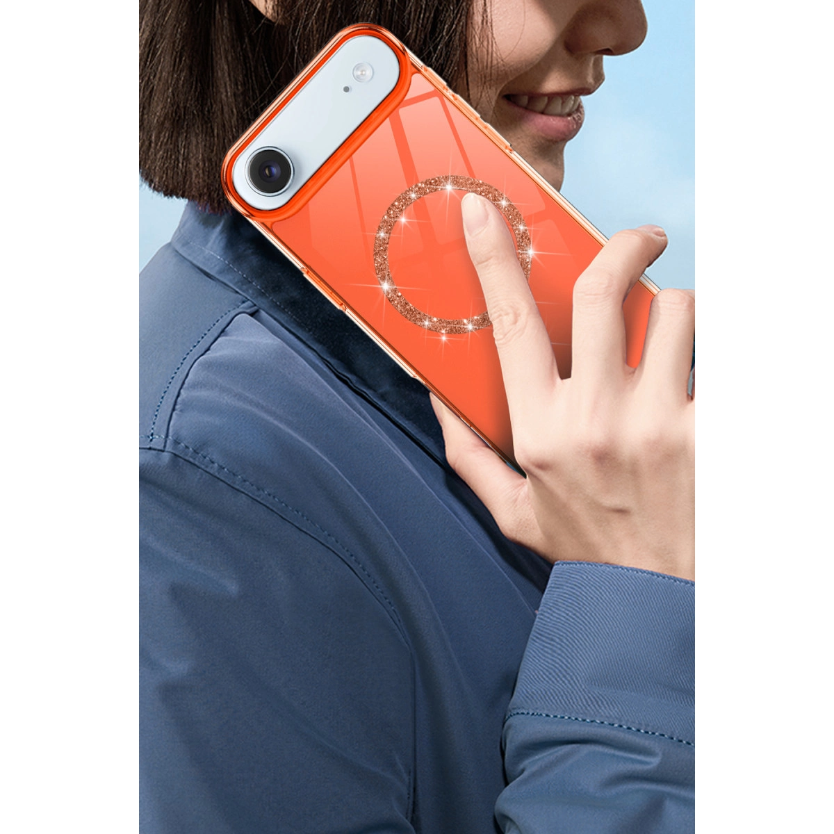 Kişi, simli halkalı turuncu bir telefon tutuyor. Arka planda mavi gökyüzü.