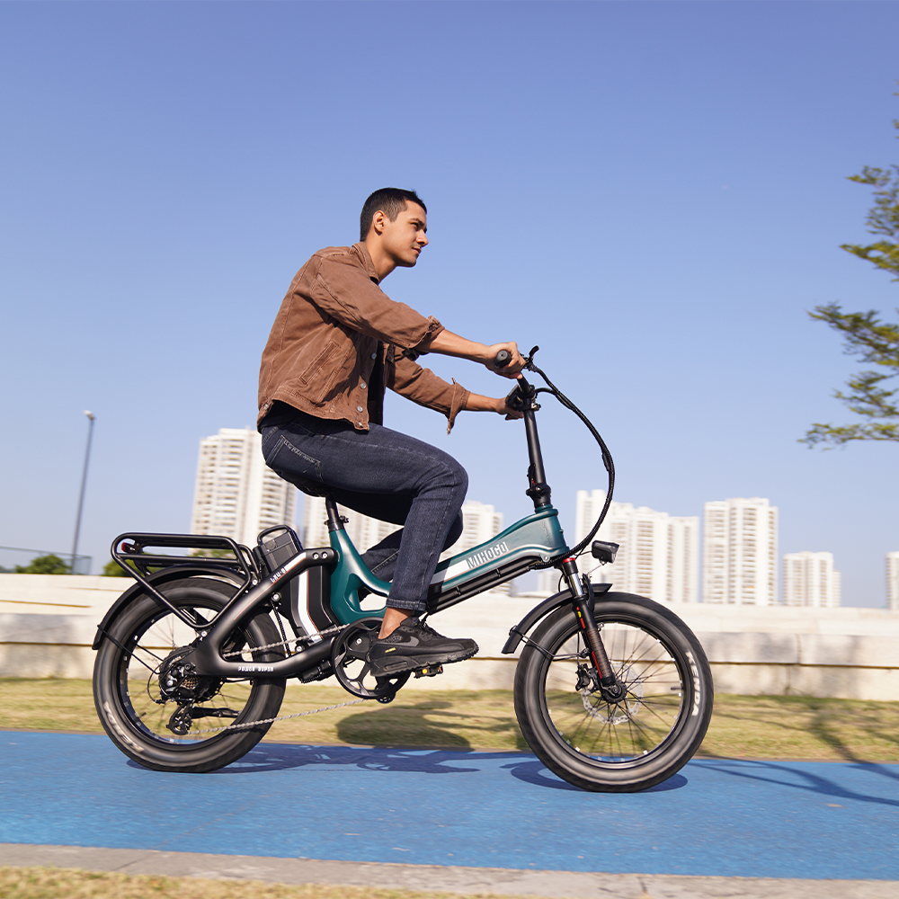 Ein Mann fährt ein grünes E-Bike auf einem blauen Weg mit Gebäuden im Hintergrund.