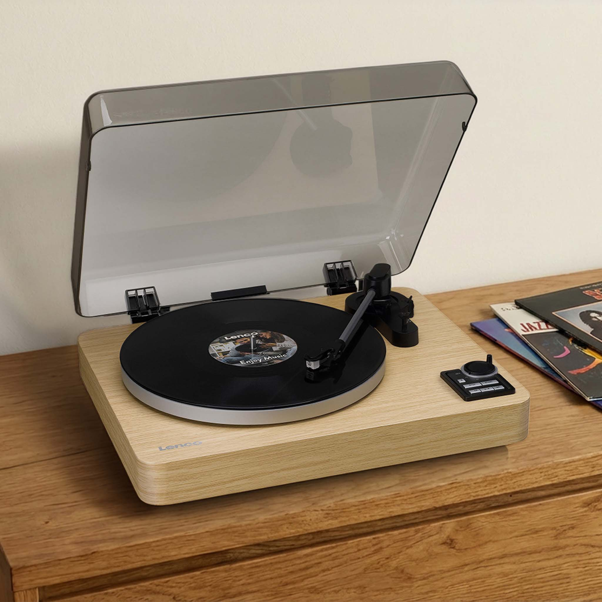 Gramofon z płytą, ramieniem i przezroczystą pokrywą na drewnianym stole.