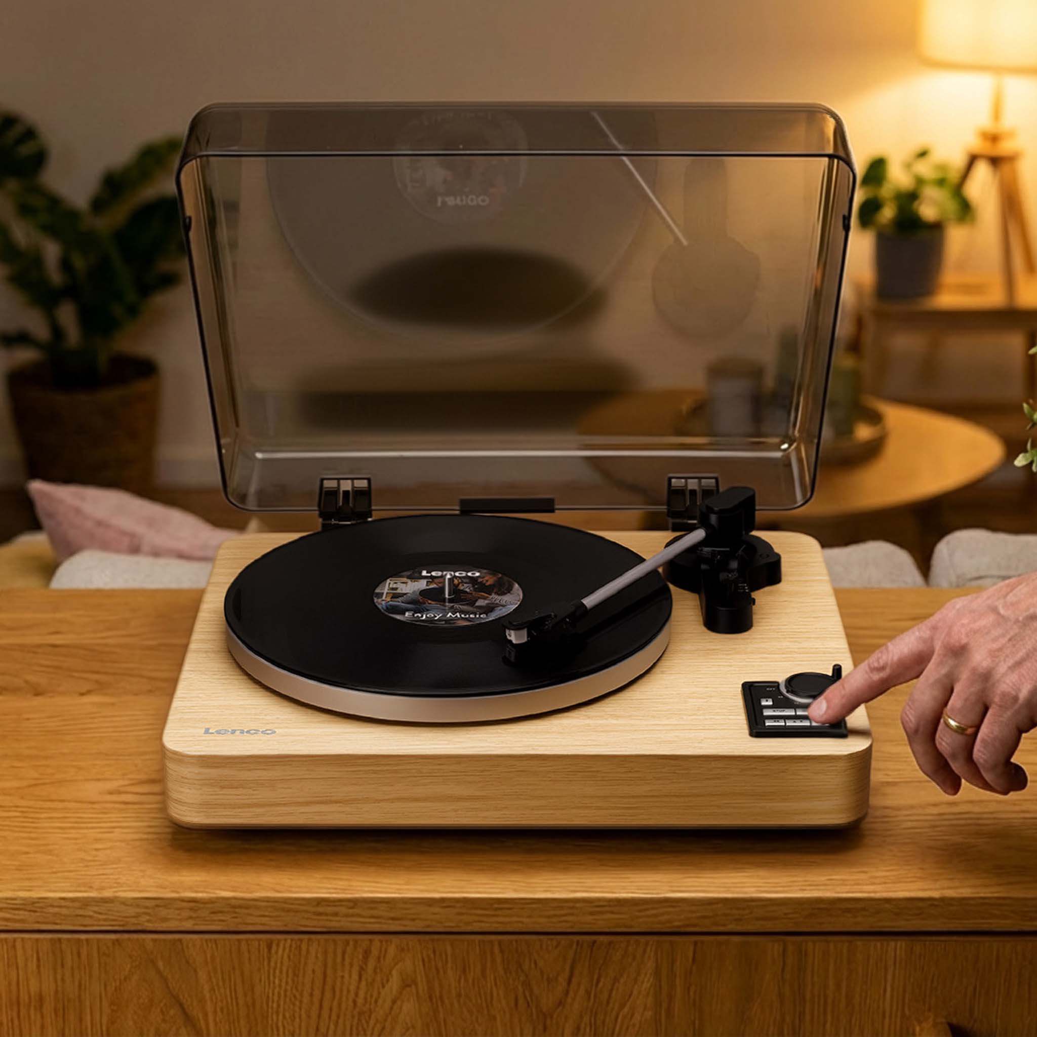 Gramofon z zamkniętą pokrywą, na drewnianym stole. Ręka go obsługuje.