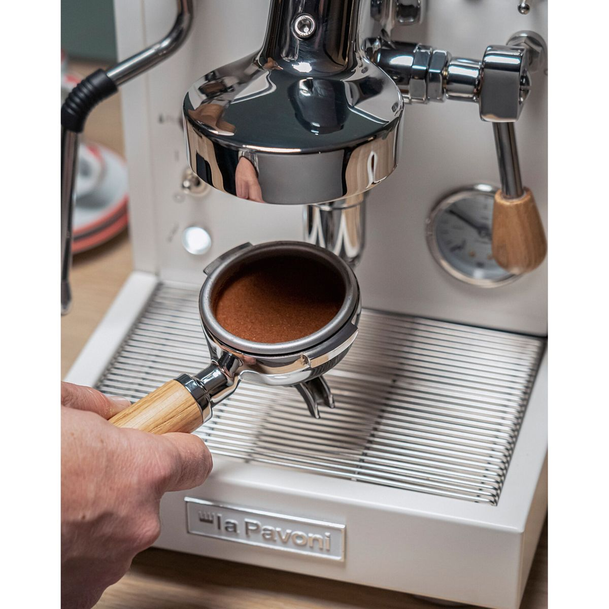 Eine Hand hält einen Siebträger mit Kaffeepulver unter einer Espressomaschine.