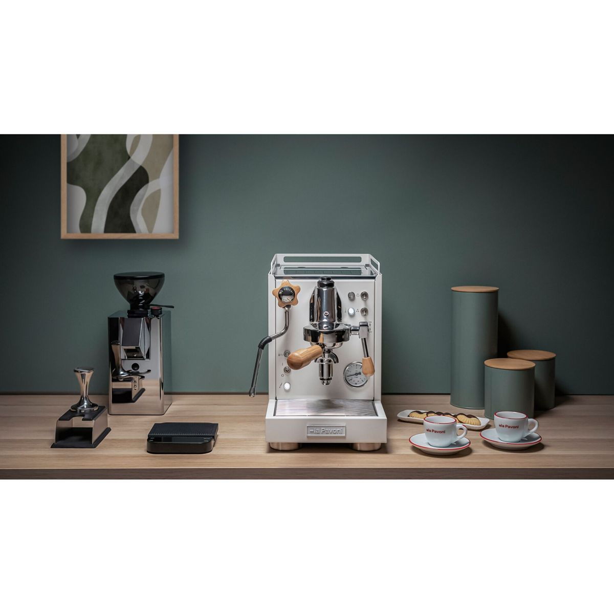 Ein weißer Espressokocher mit Kaffeemühle, Tamper und Tassen auf einem Holztisch.