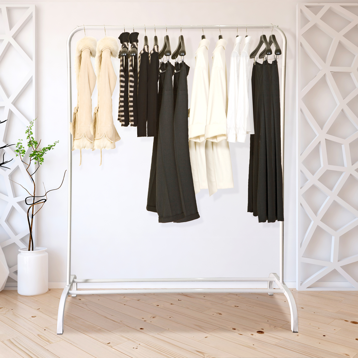 Perchero con ropa negra, blanca y beige contra una pared blanca.