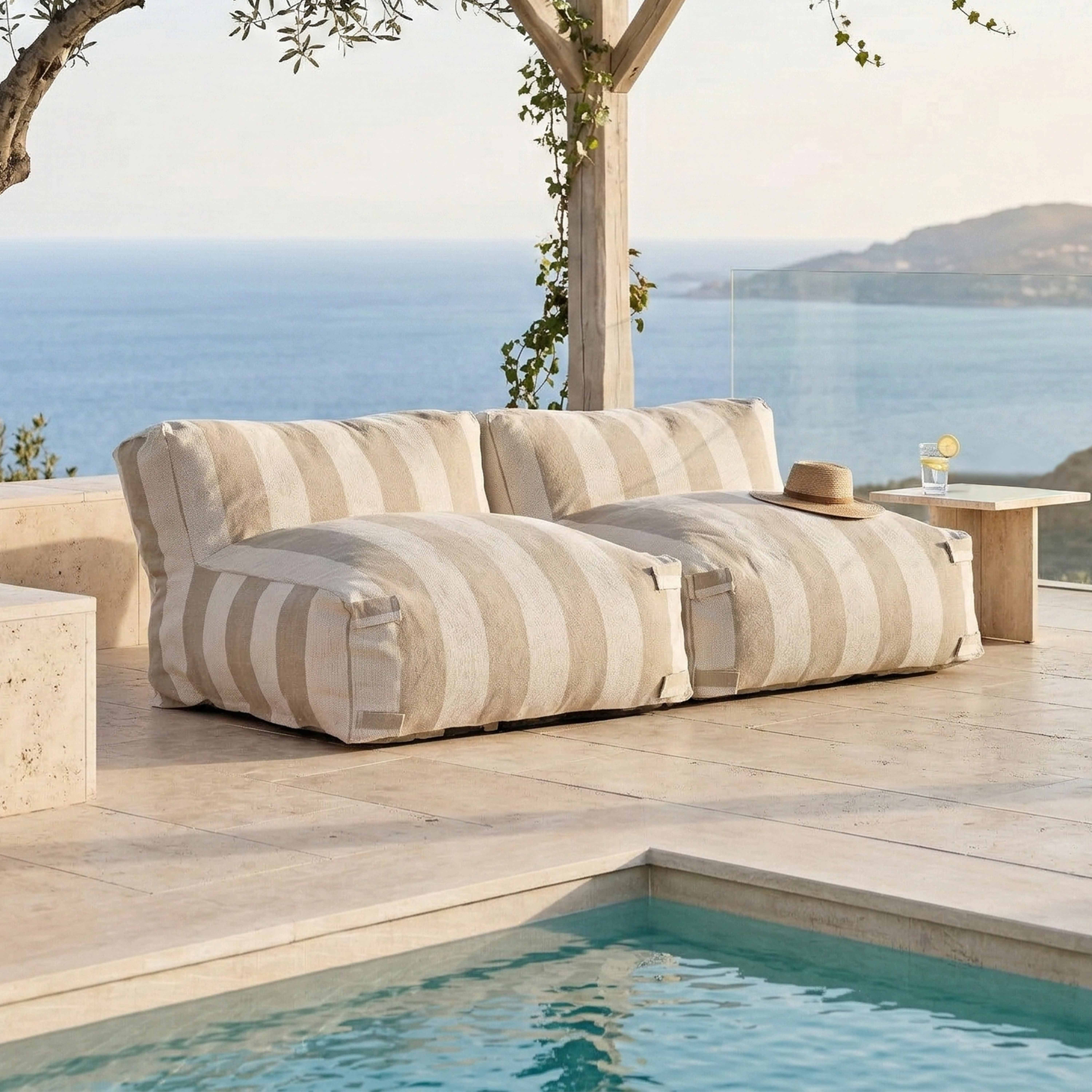 Gestreifte Couch am Pool mit Meerblick, ein Hut liegt auf der Couch.